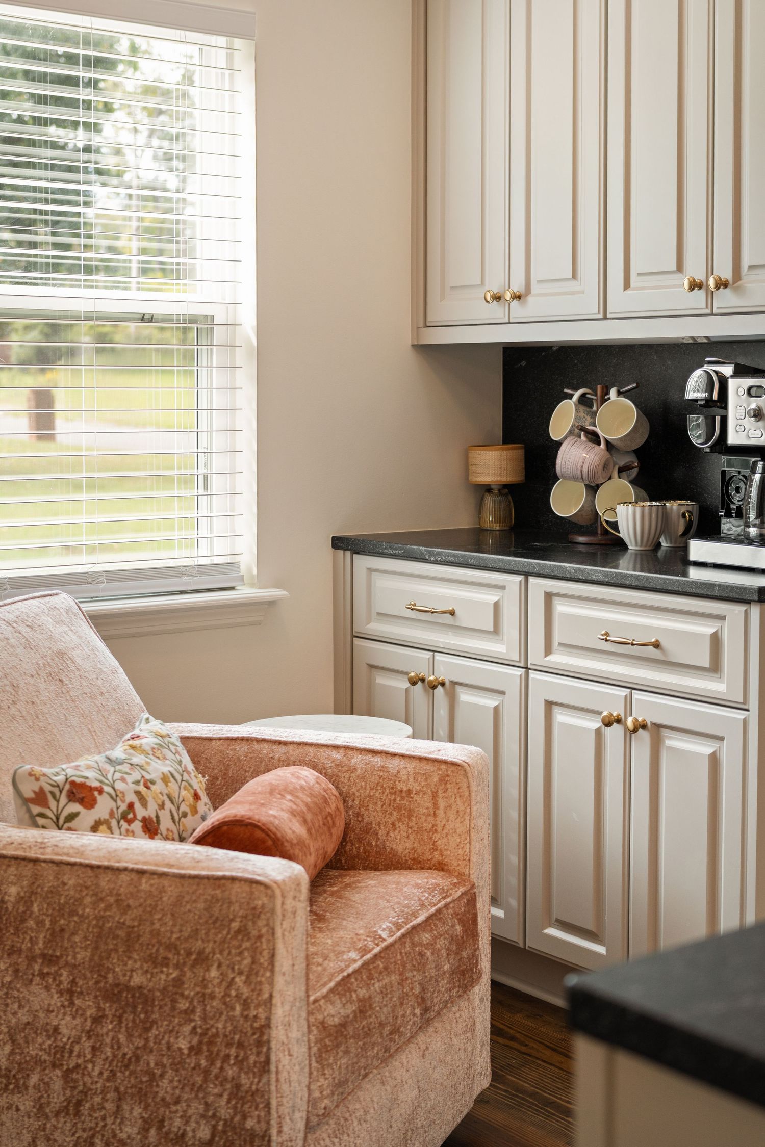 Elegant kitchen nook with cream cabinets and coral velvet bench seating beneath window for real estate photography in Augusta, GA.