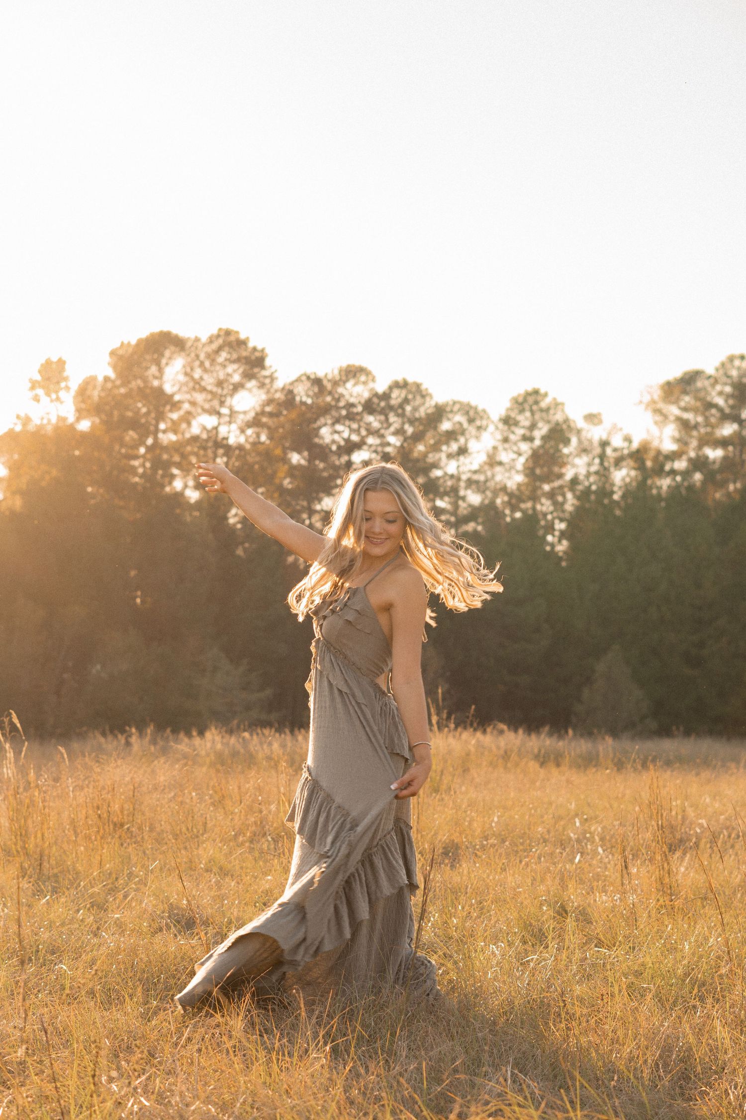 Woman in flowy dress twirling in golden field during sunset with trees in background in Augusta, GA.