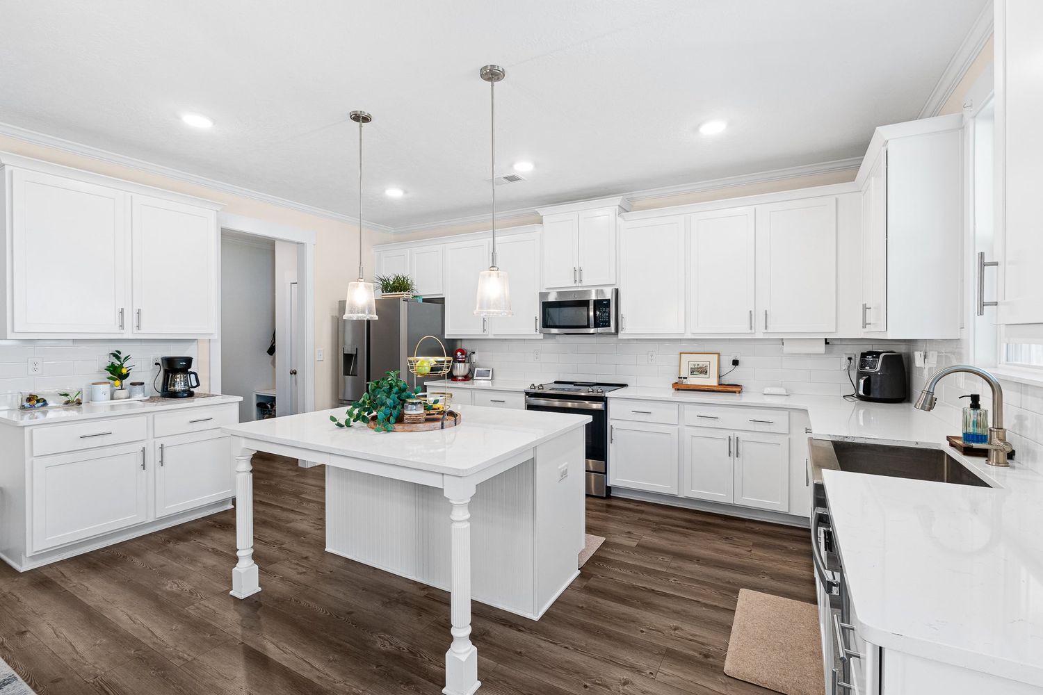 Contemporary white kitchen with center island, recessed lighting, and dark wood flooring for real estate photography in Augusta, GA.