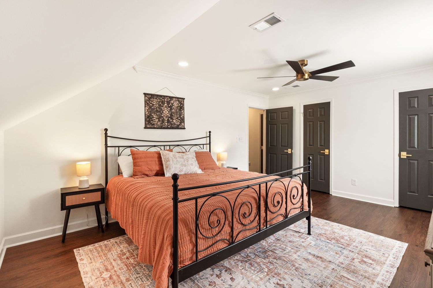 Modern bedroom with wrought iron bed frame, ceiling fan, and warm orange bedding for real estate photography in Augusta, GA.