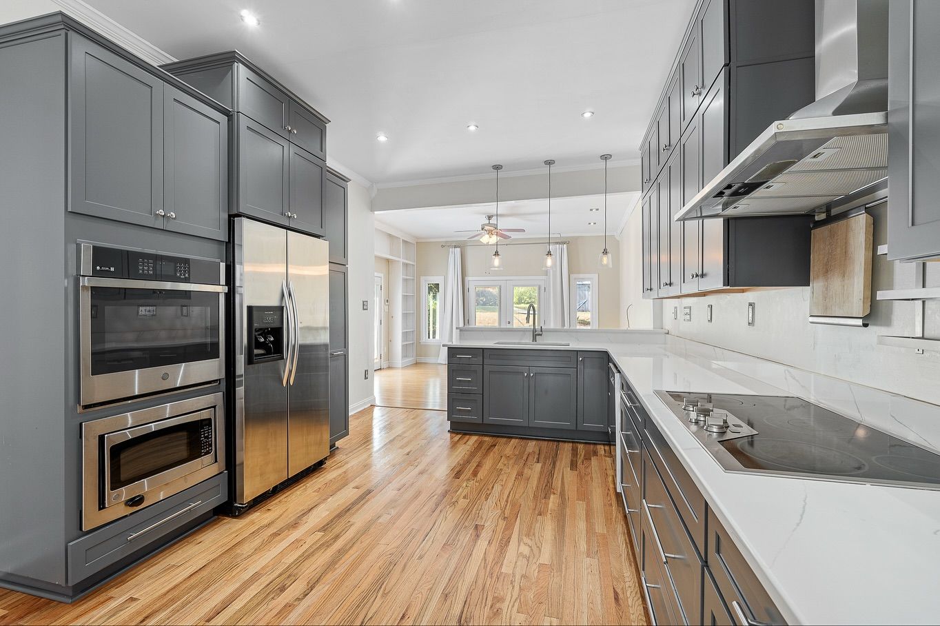Modern kitchen with gray cabinets, stainless steel appliances, and hardwood floors in an open concept layout for real estate photography.