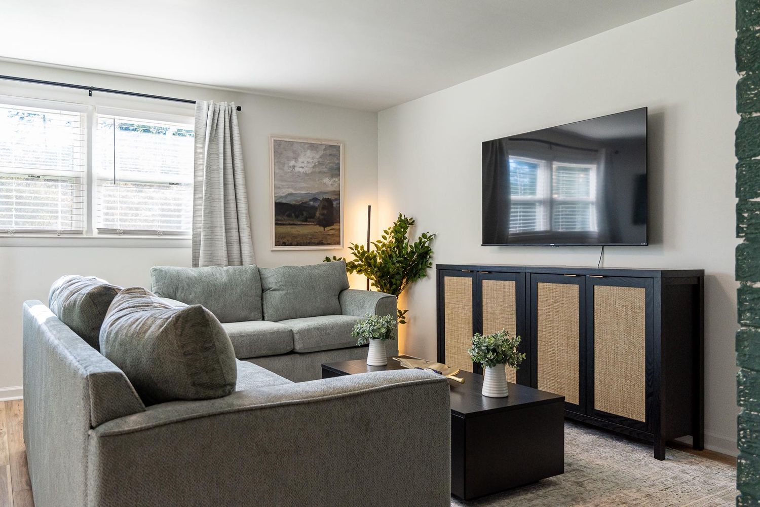 Cozy living room with mounted TV, gray sectional sofa, and natural light from windows for real estate photography in Augusta, GA.