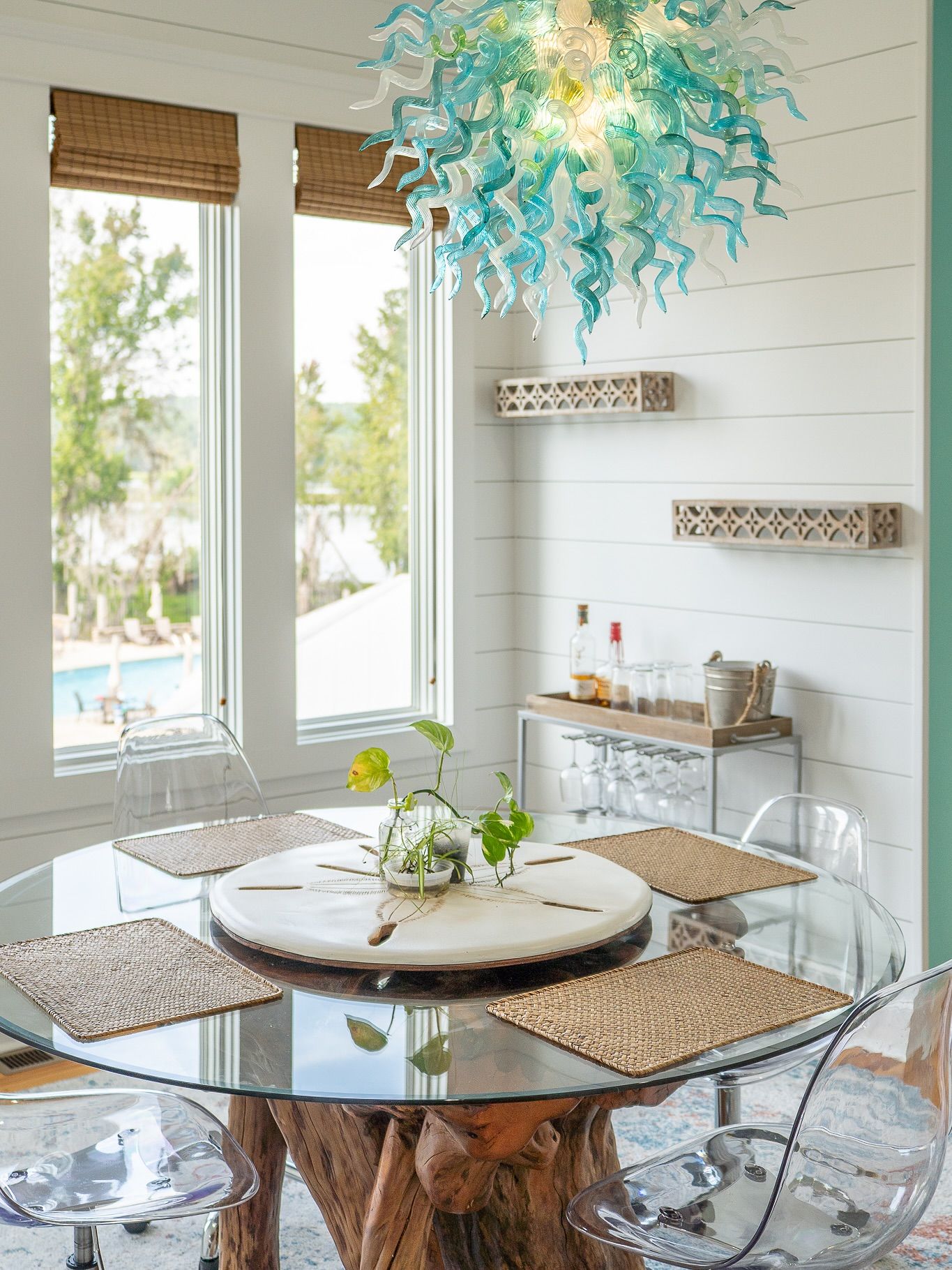 Coastal dining nook with round table, ghost chairs, and turquoise chandelier against white shiplap walls for real estate photography in GA.