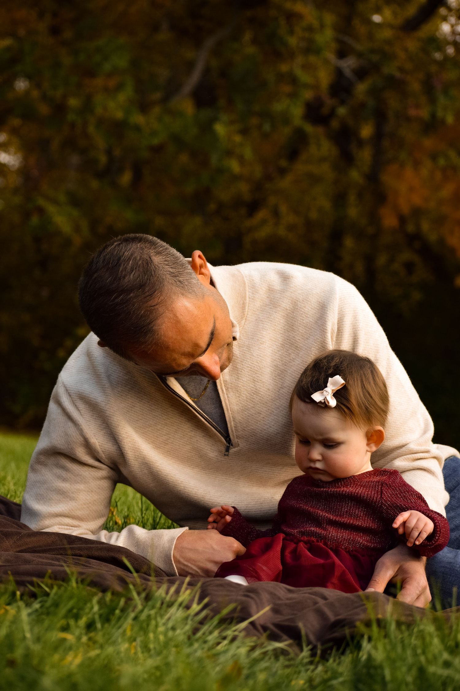 Tender moment captured on grass with autumn trees in background.