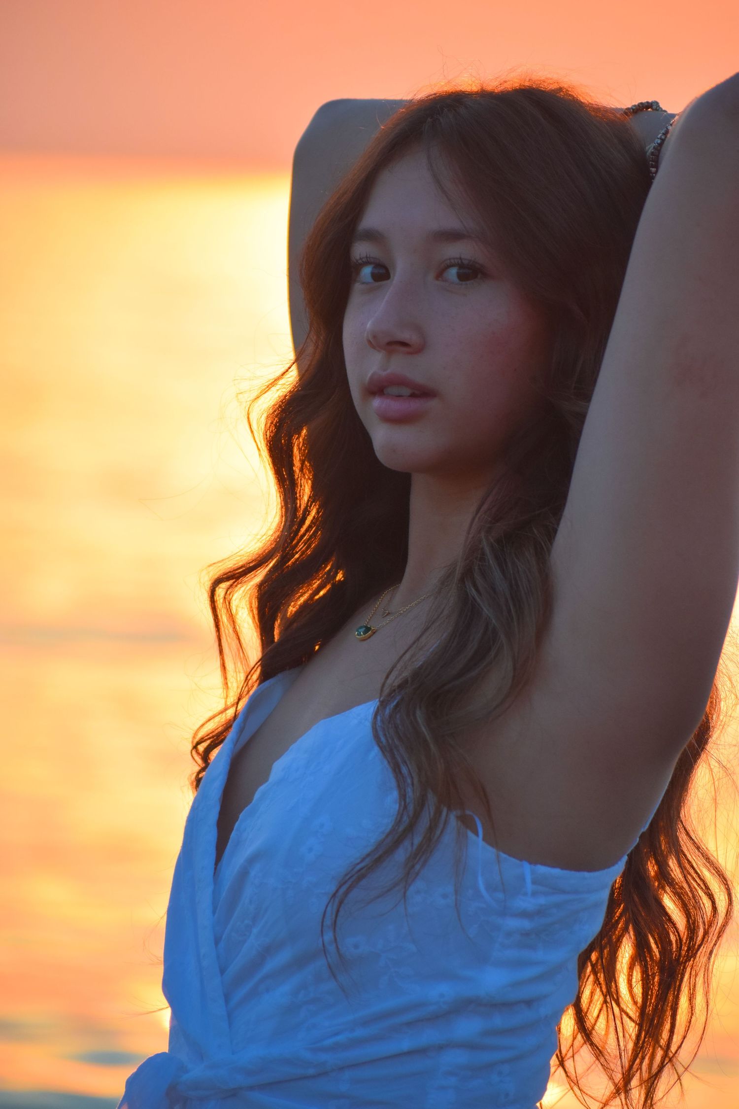 Woman in blue dress poses at sunset with golden light illuminating her long dark hair.