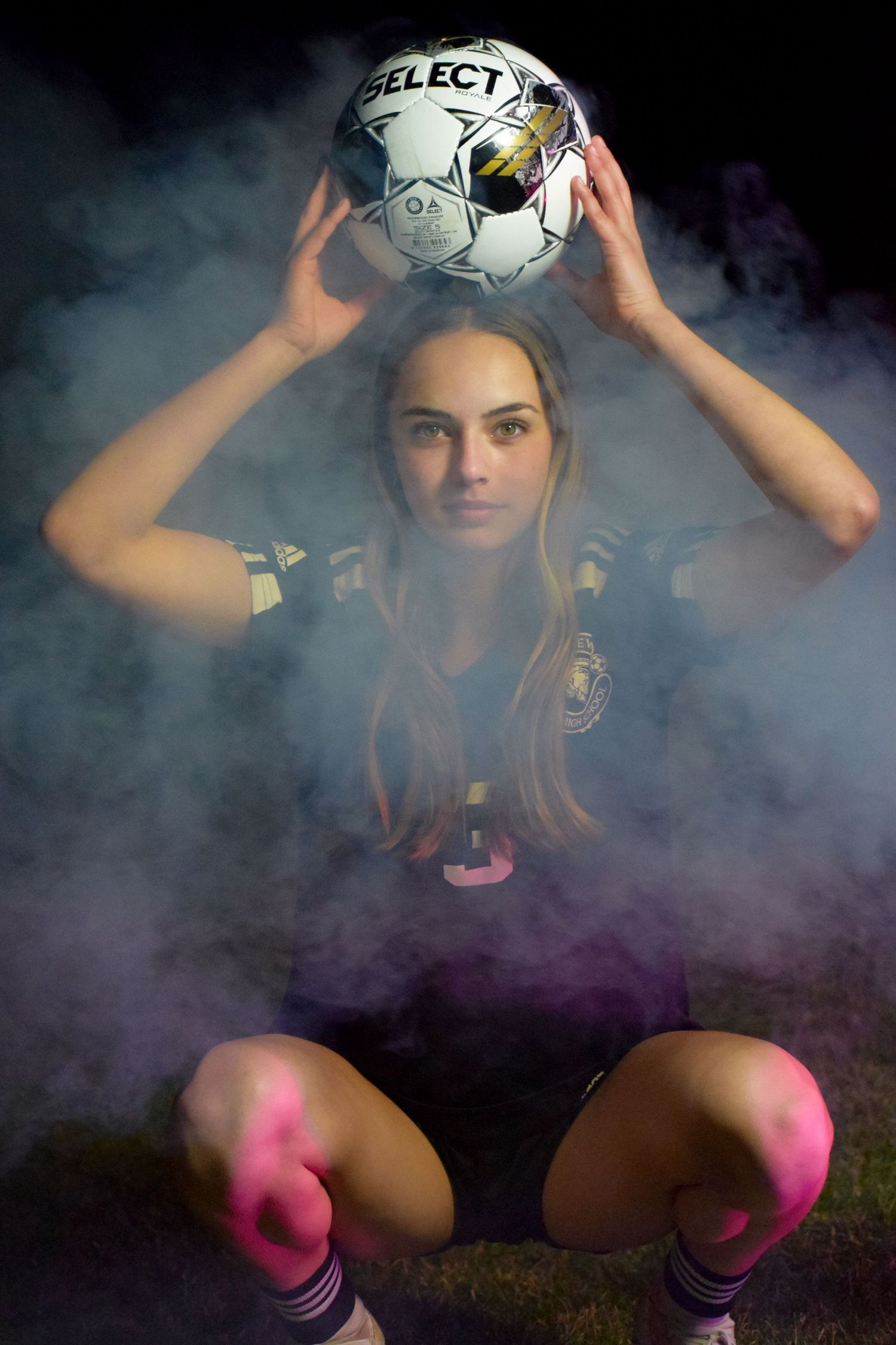 Soccer player posing with ball amidst dramatic purple smoke effects.