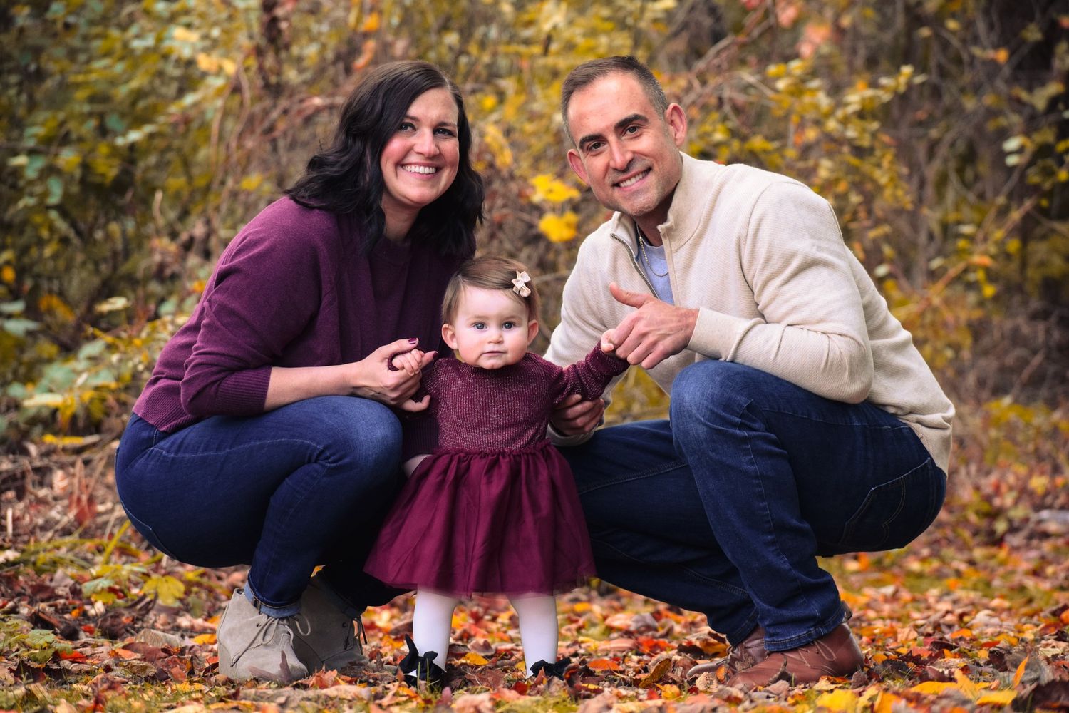 Happy family moment photographed in autumn setting with fallen leaves.