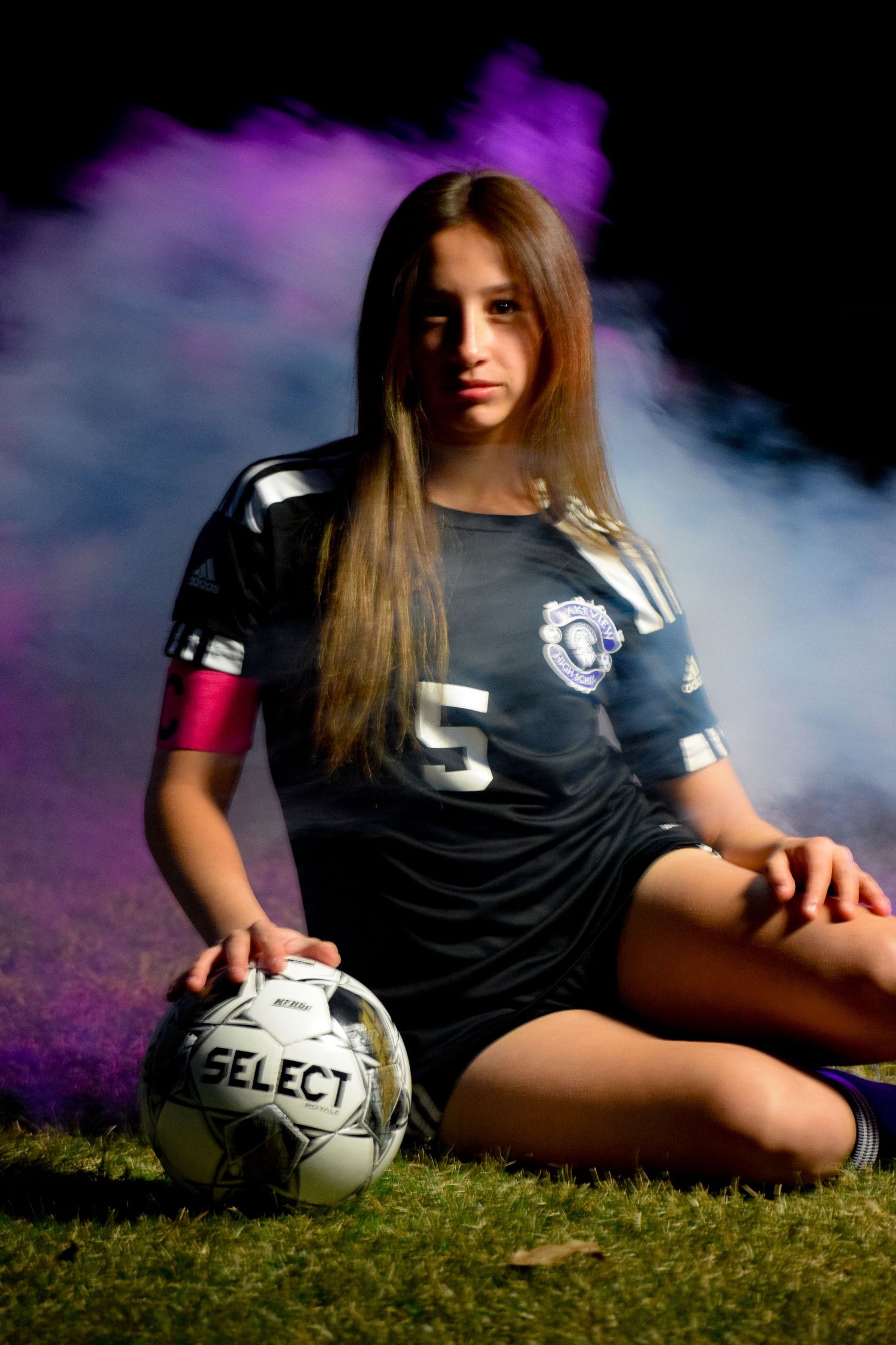 Soccer player reclining on grass with Select ball in moody lighting.