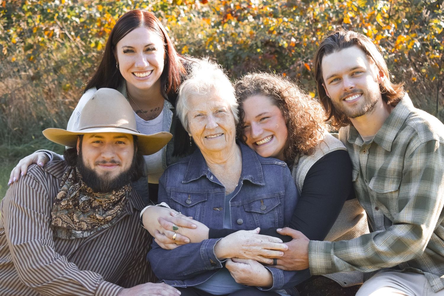 Cheerful group photo with people embracing under autumn trees with golden leaves.