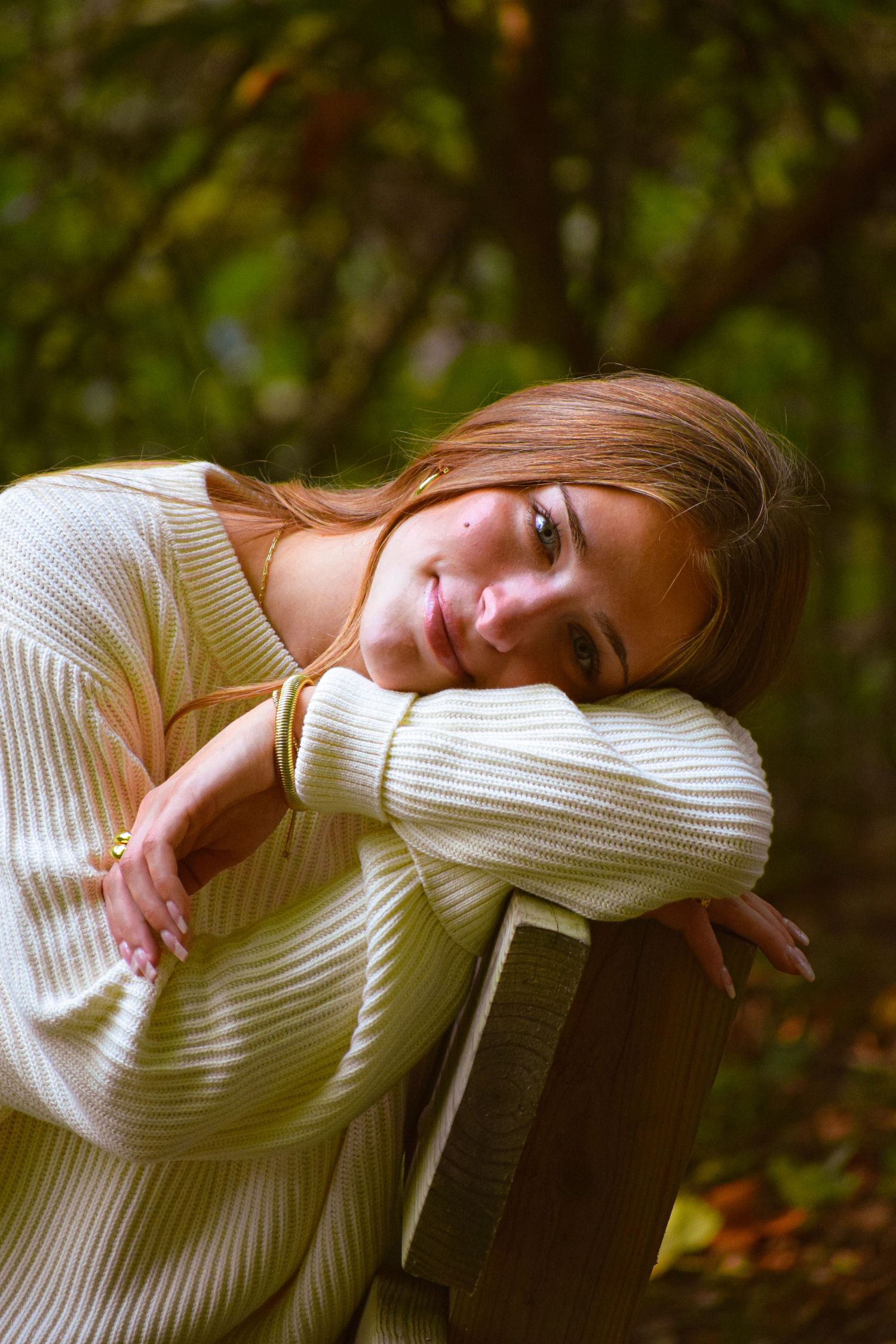 Person in cream sweater rests head on arms in autumn outdoor setting.
