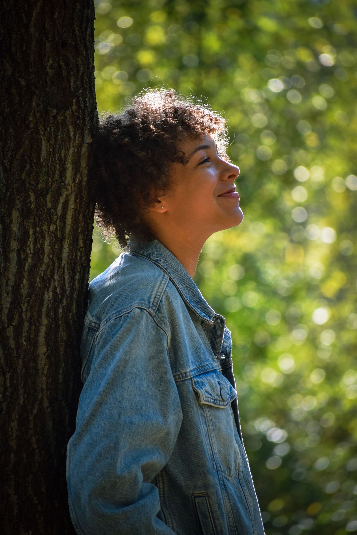 Silhouette against sunlit forest background wearing denim jacket in profile view.
