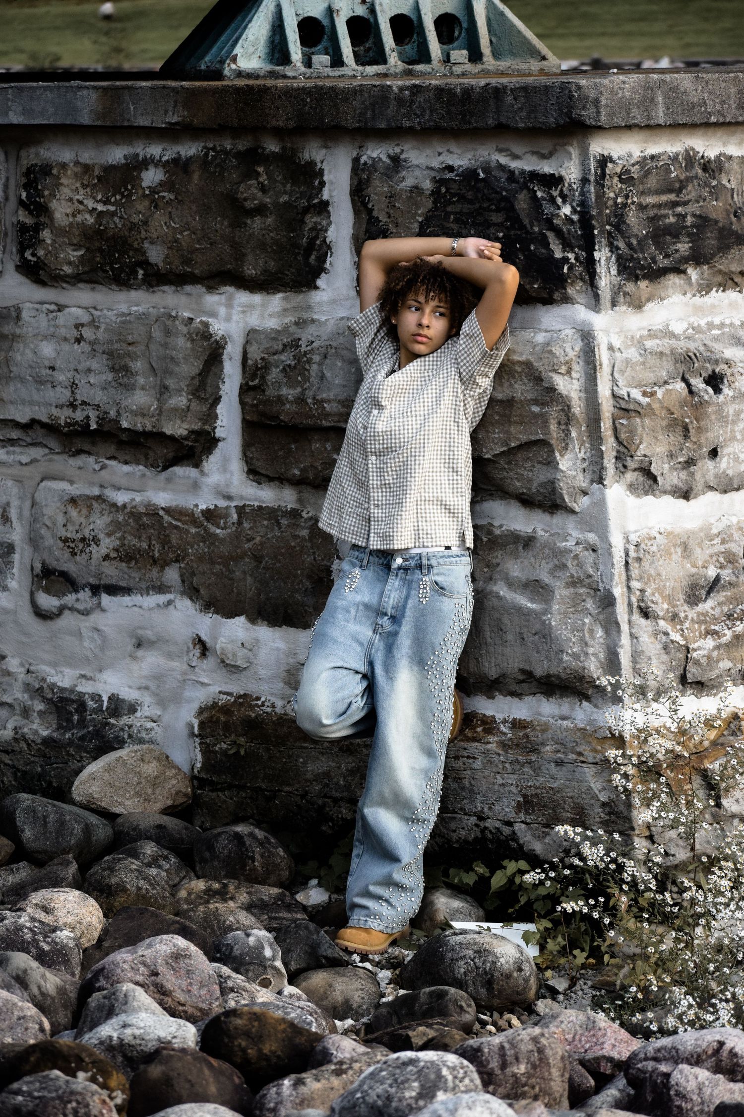 Person in casual attire leaning against stone wall with rocks at base.
