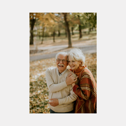 Elderly couple sharing a joyful moment together while sitting outdoors among fallen autumn leaves.