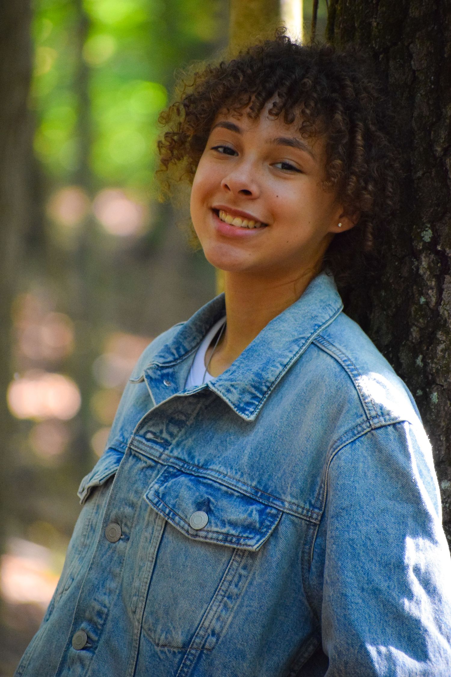 Casual portrait in a denim jacket against a soft-focus forest background.