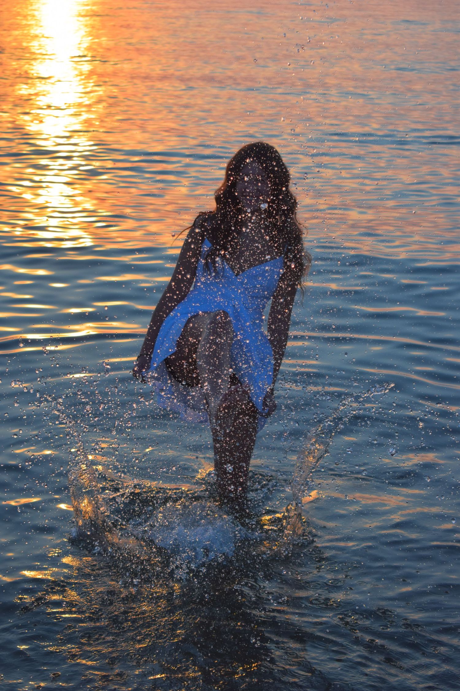 Person splashing in ocean water creates dynamic spray during sunset.