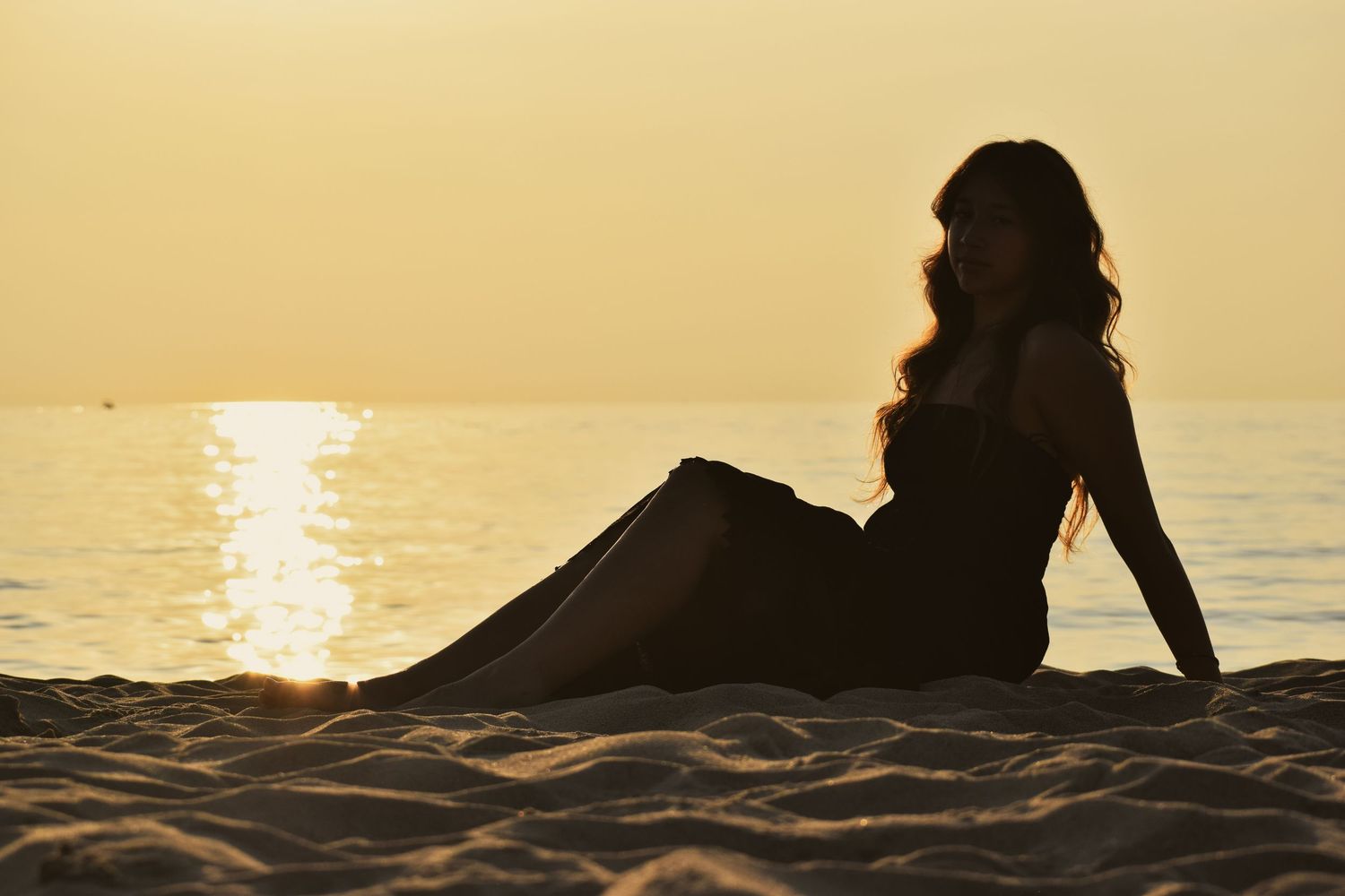 Silhouette of person relaxing on beach at sunset with golden light reflecting on water.