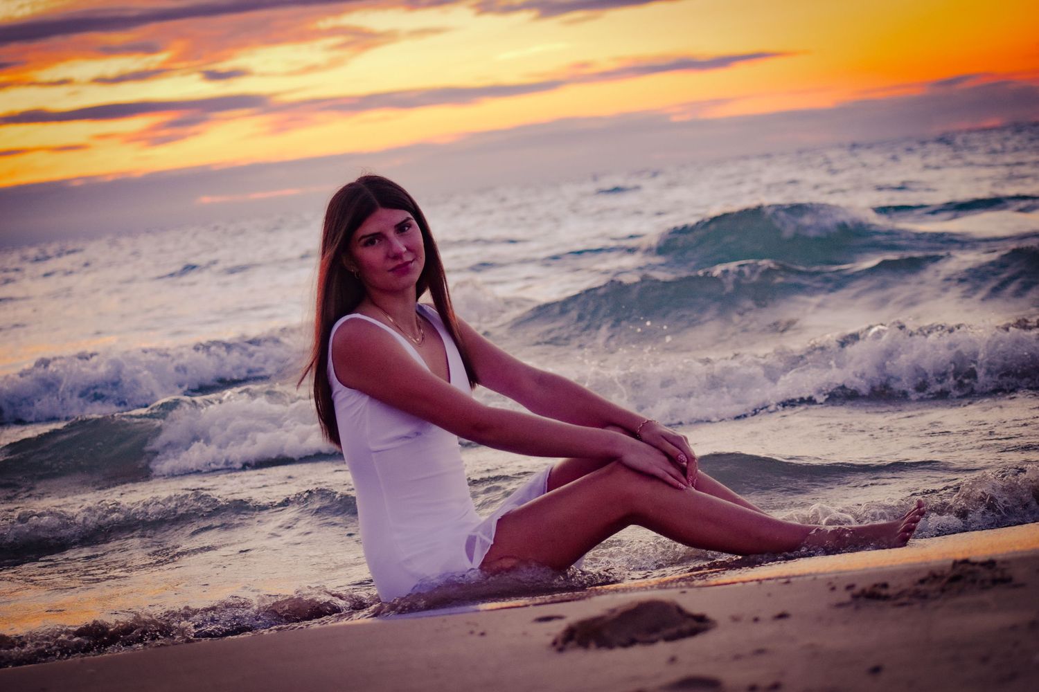 Model poses on beach during golden hour as waves crash behind.