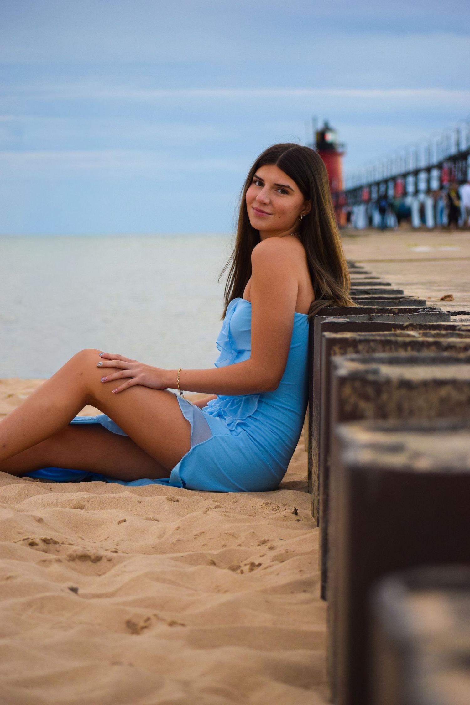 Woman in blue dress poses on sandy beach near wooden pier during sunset photoshoot.