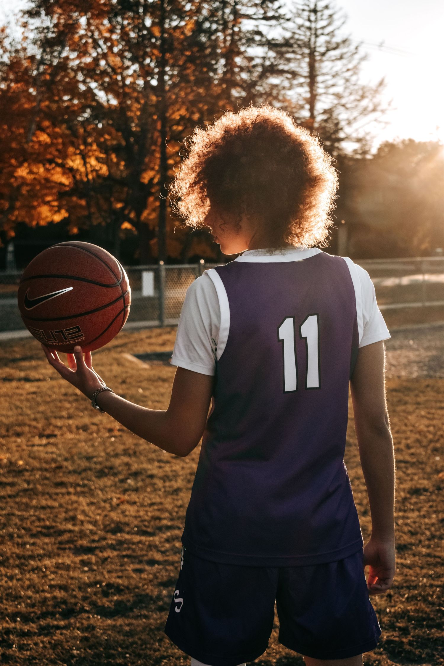 Silhouette of basketball player holding ball against golden sunset with autumn trees.