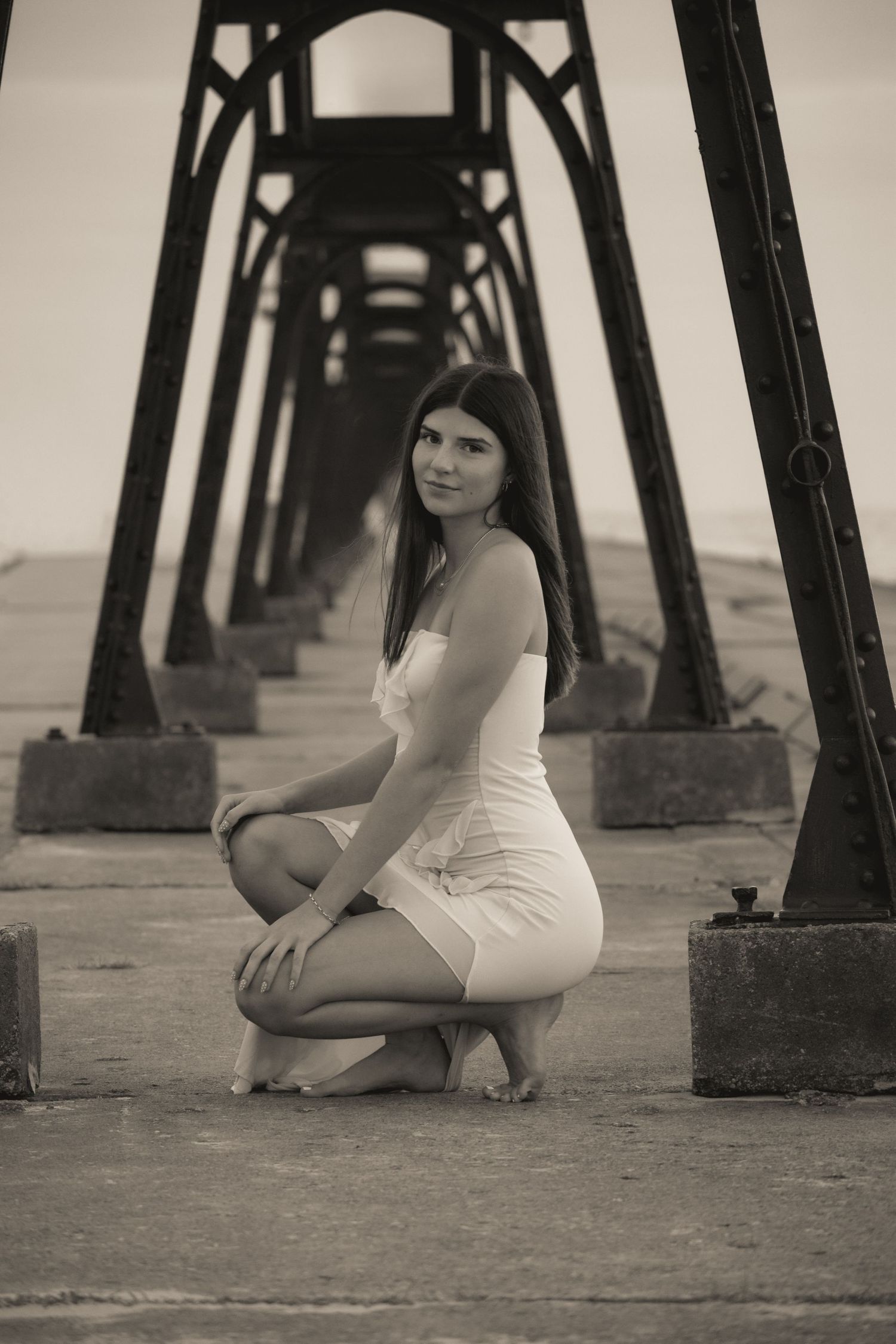 Black and white portrait under pier support beams creating dramatic architectural framing.