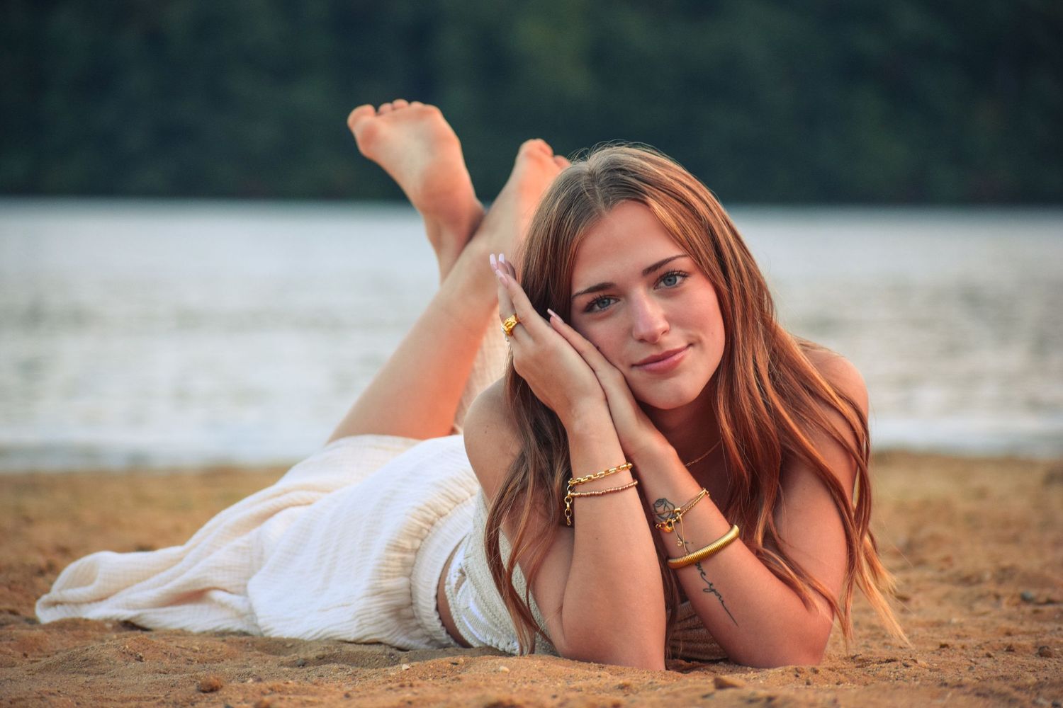 Person in white dress lying on sandy beach during golden hour.