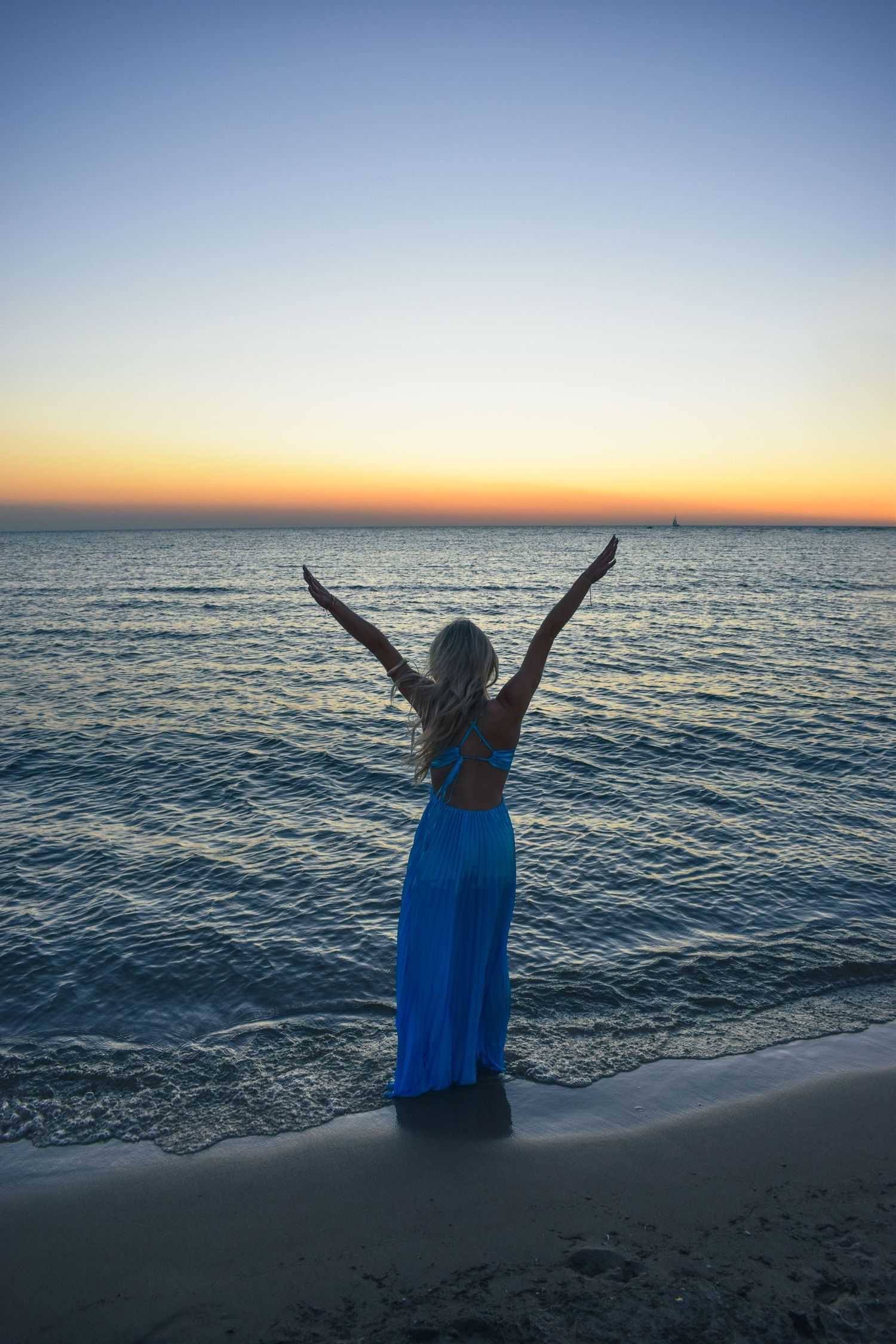 Silhouette of someone with arms raised against ocean sunset backdrop.