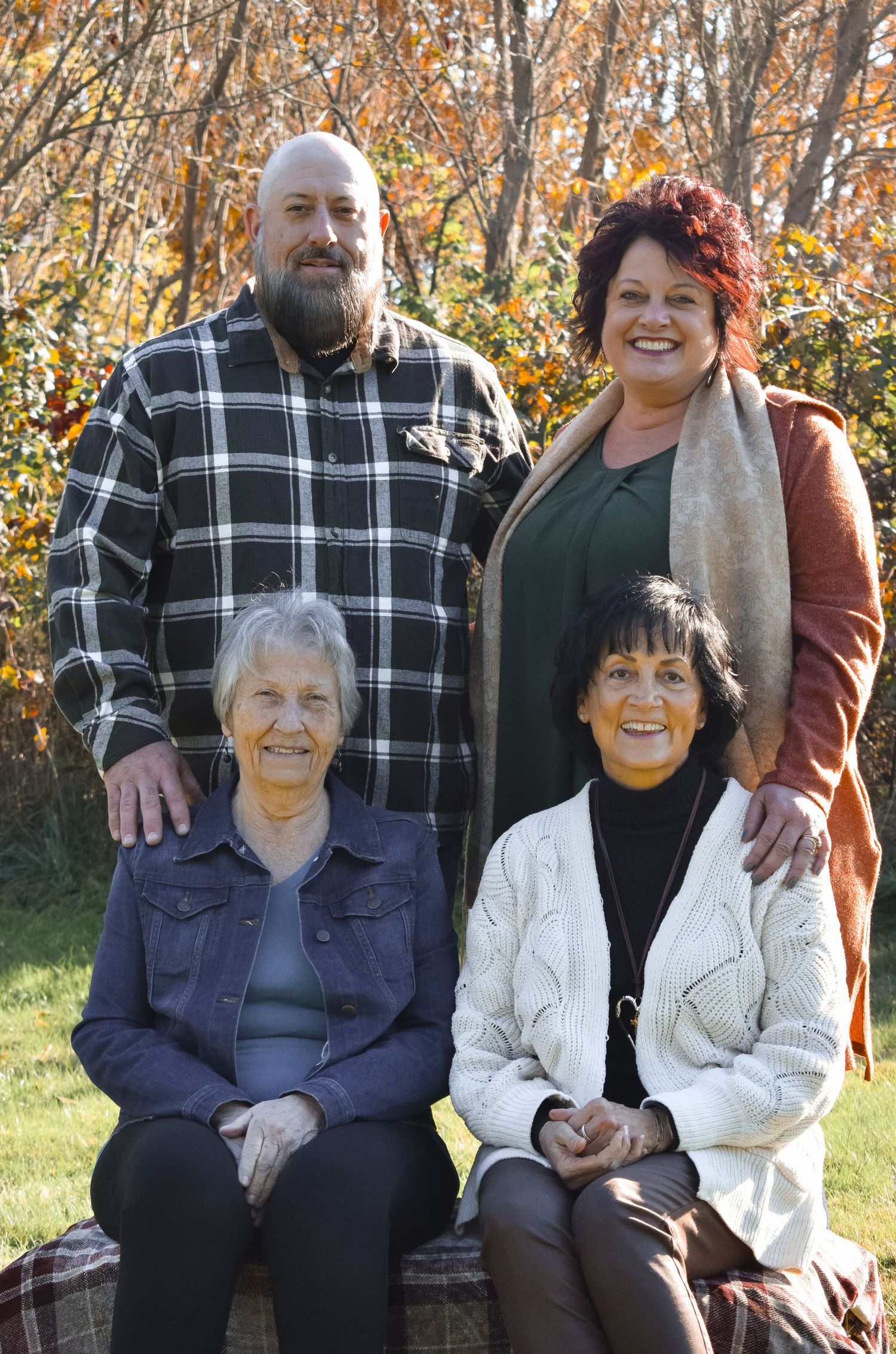 Casual outdoor family gathering with people seated together against a backdrop of fall trees.