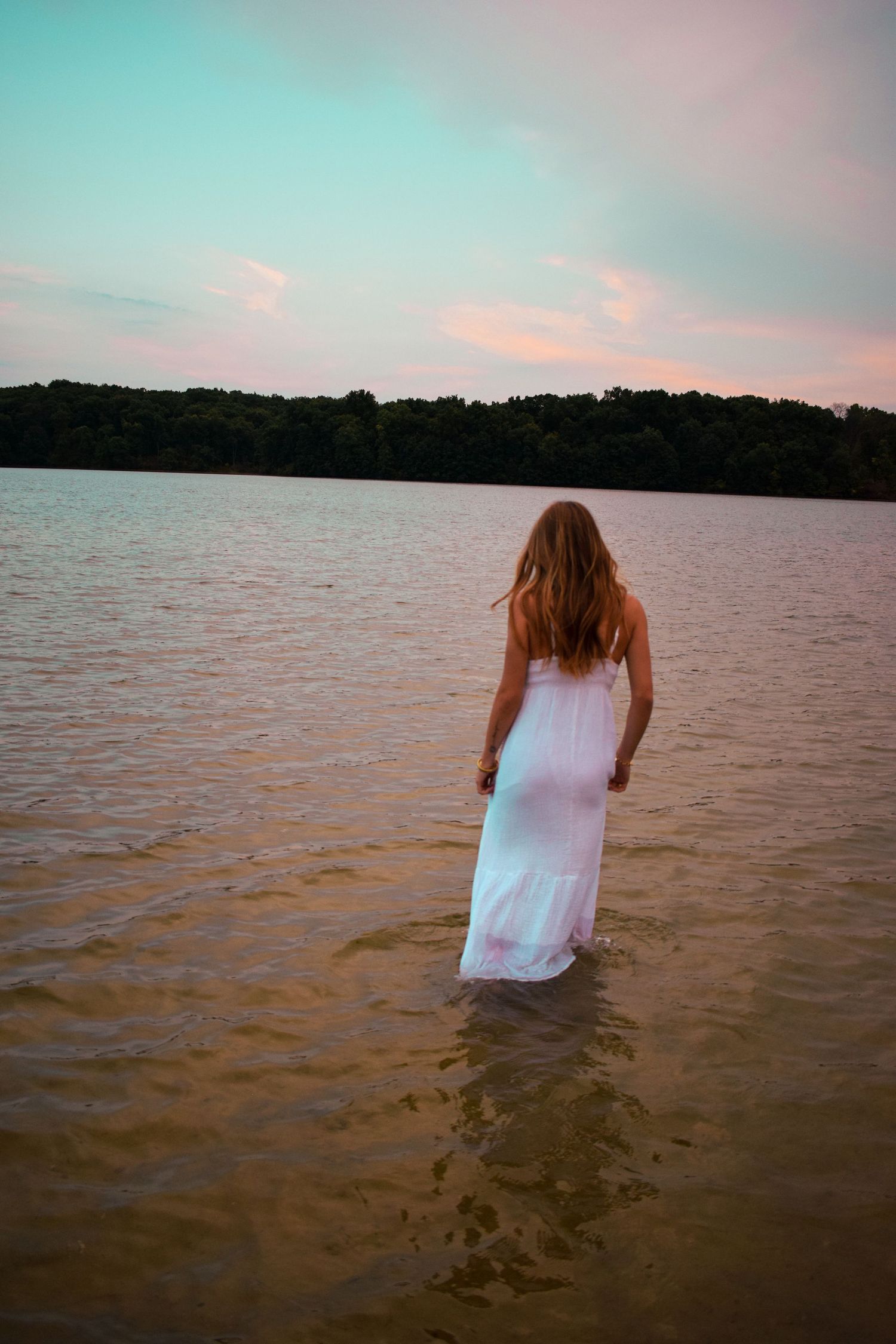 A person wading into calm waters at sunset creating a peaceful lakeside scene.