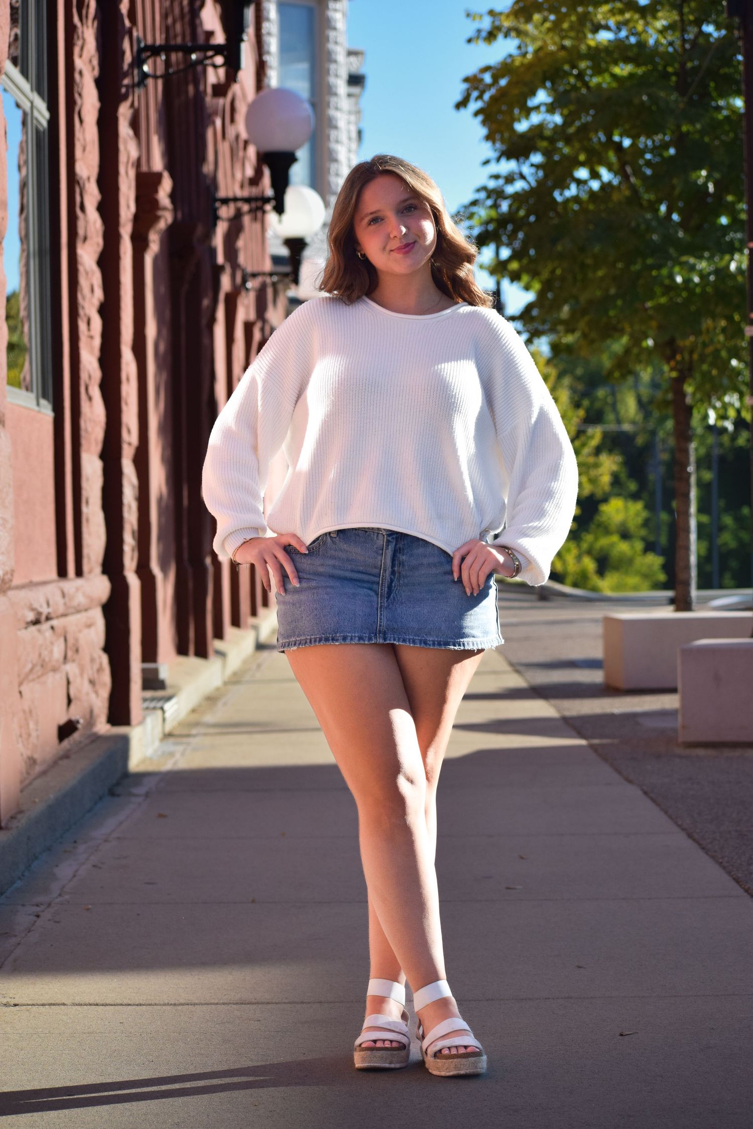 Stylish white sweater and denim shorts outfit photographed along a brick building walkway in autumn.