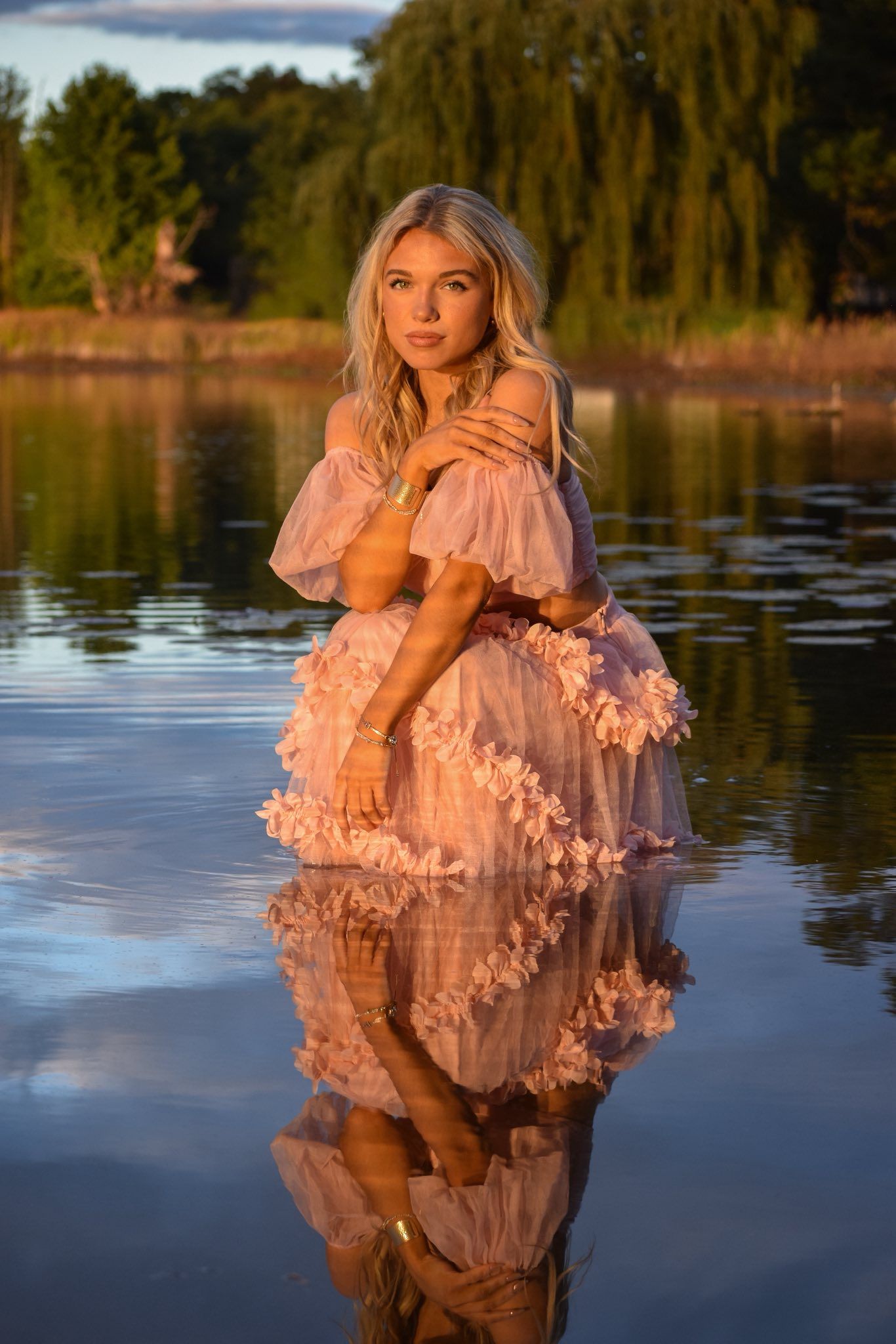 Pink dress reflects beautifully in calm lake water during golden hour photoshoot.