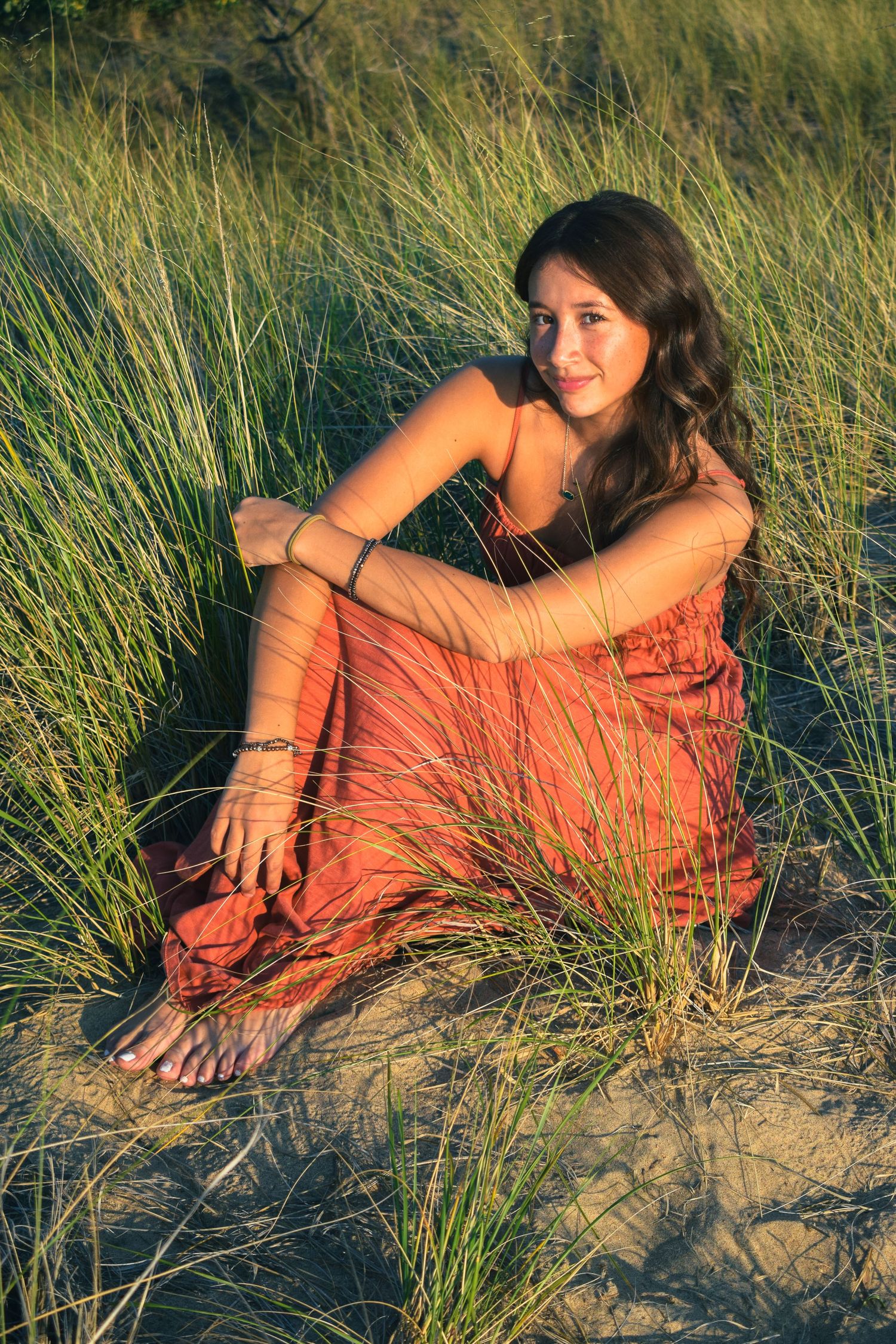 Woman in coral dress poses gracefully among tall beach grass during golden hour photo session.