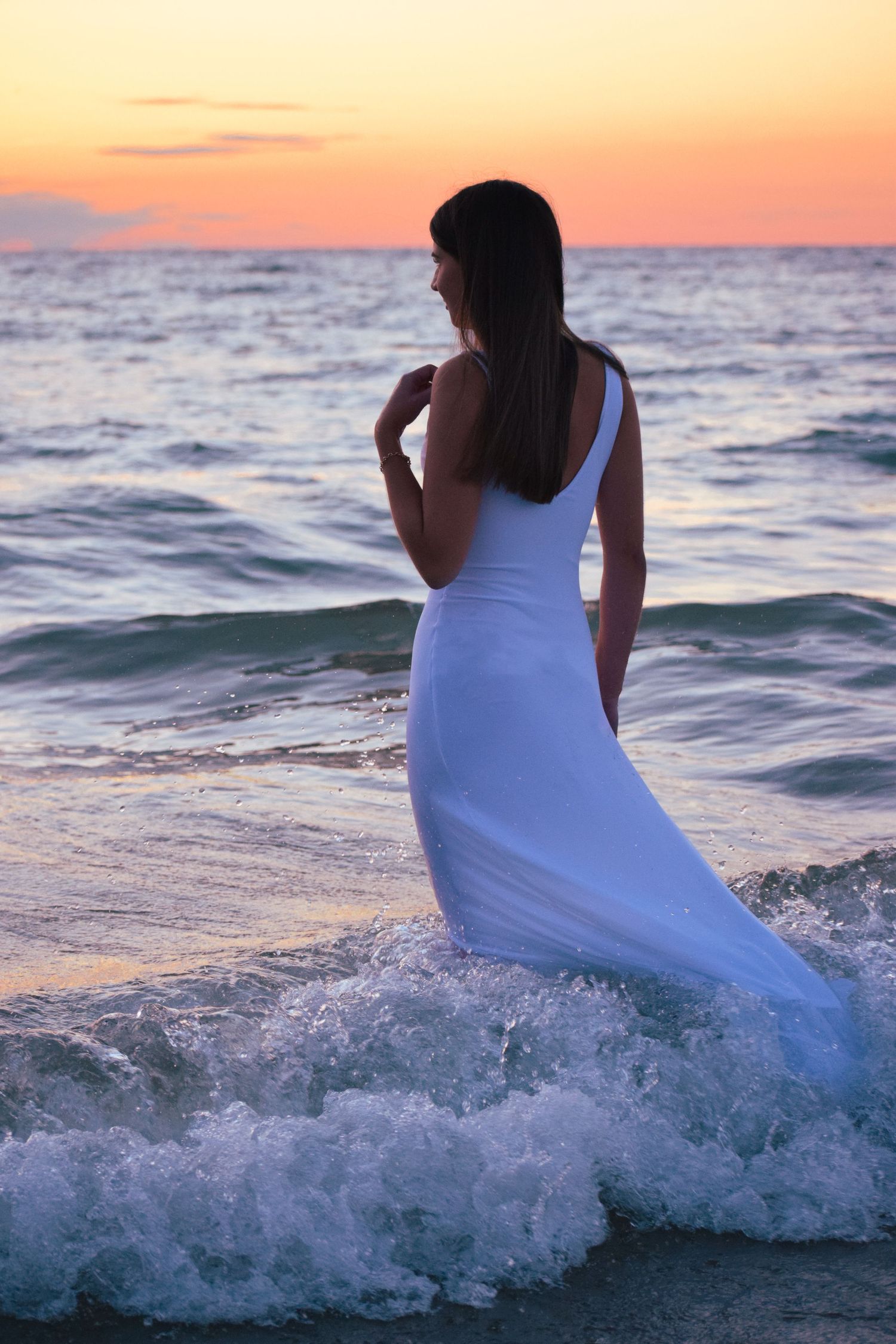 White dress flows in ocean waves during sunset beach photography session.