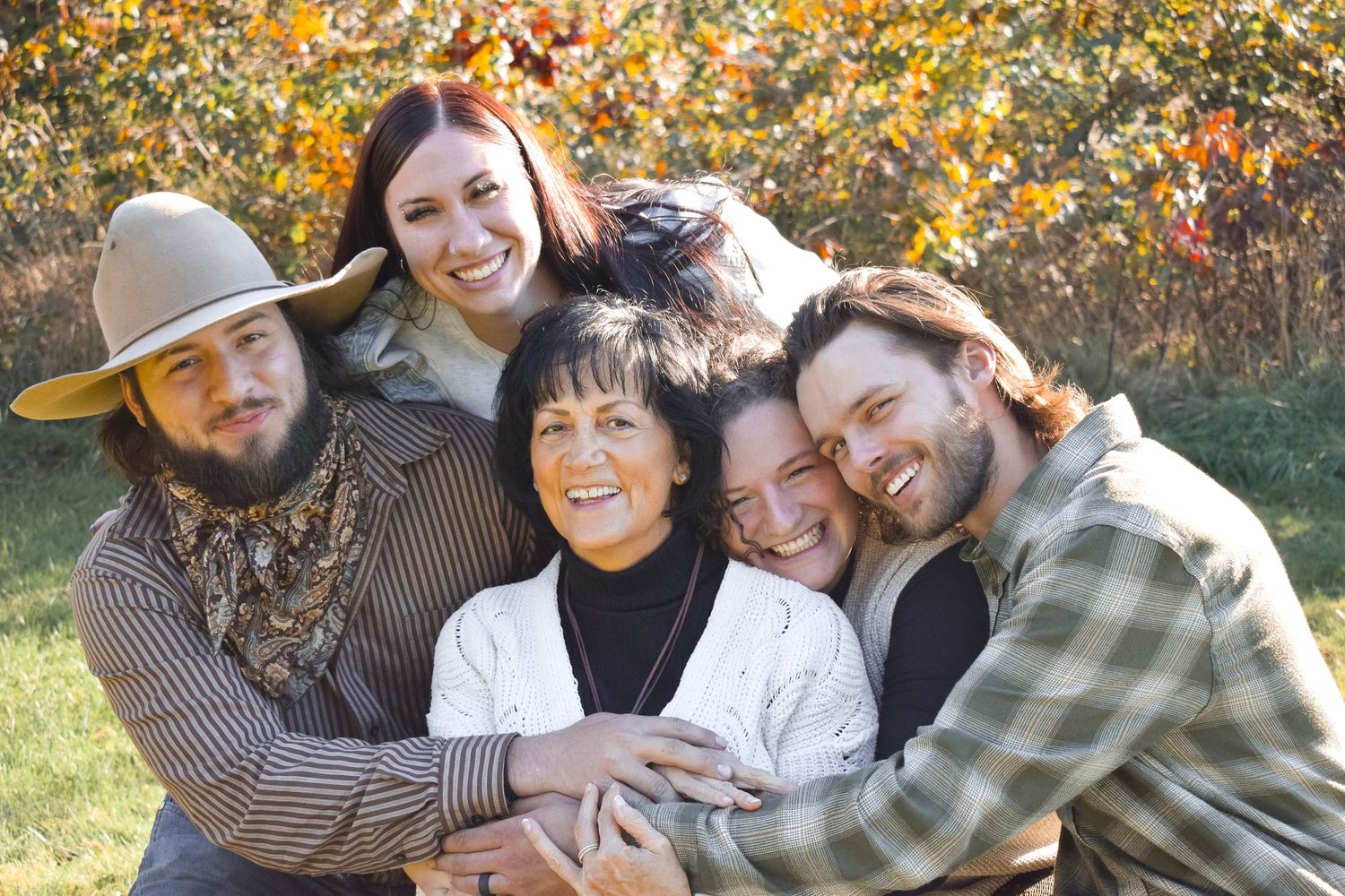 Family members hugging and smiling together during an outdoor fall photoshoot.