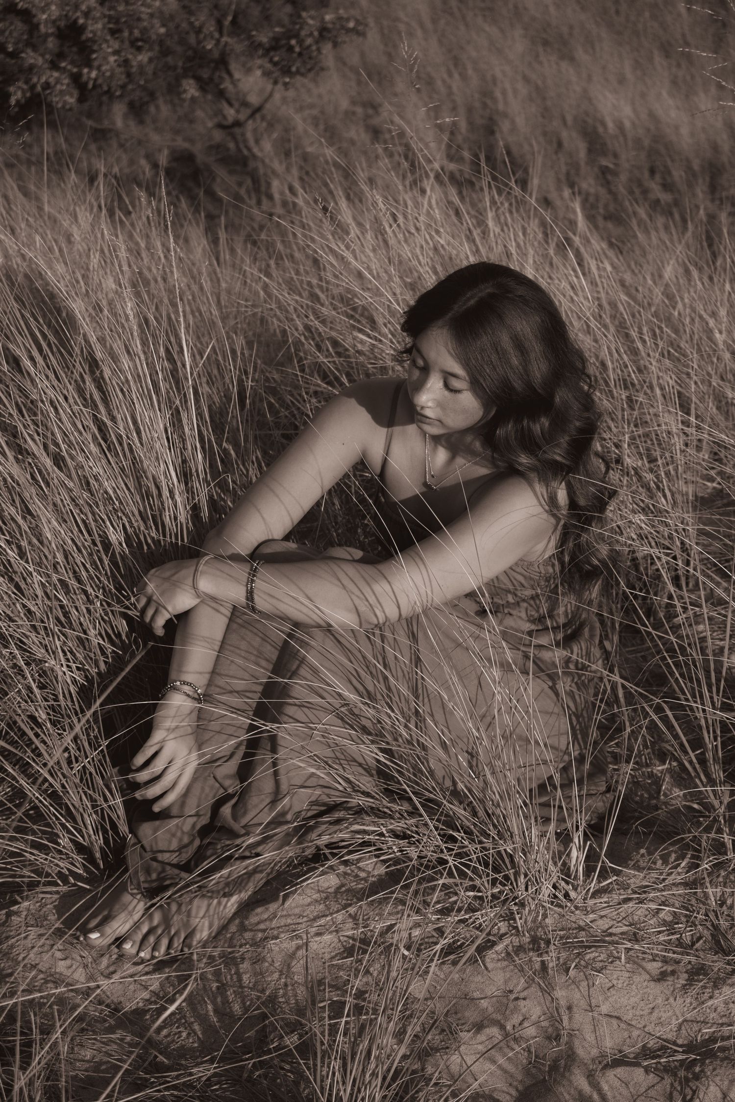 Artistic black and white portrait of woman reclining in tall grass with dramatic shadows.