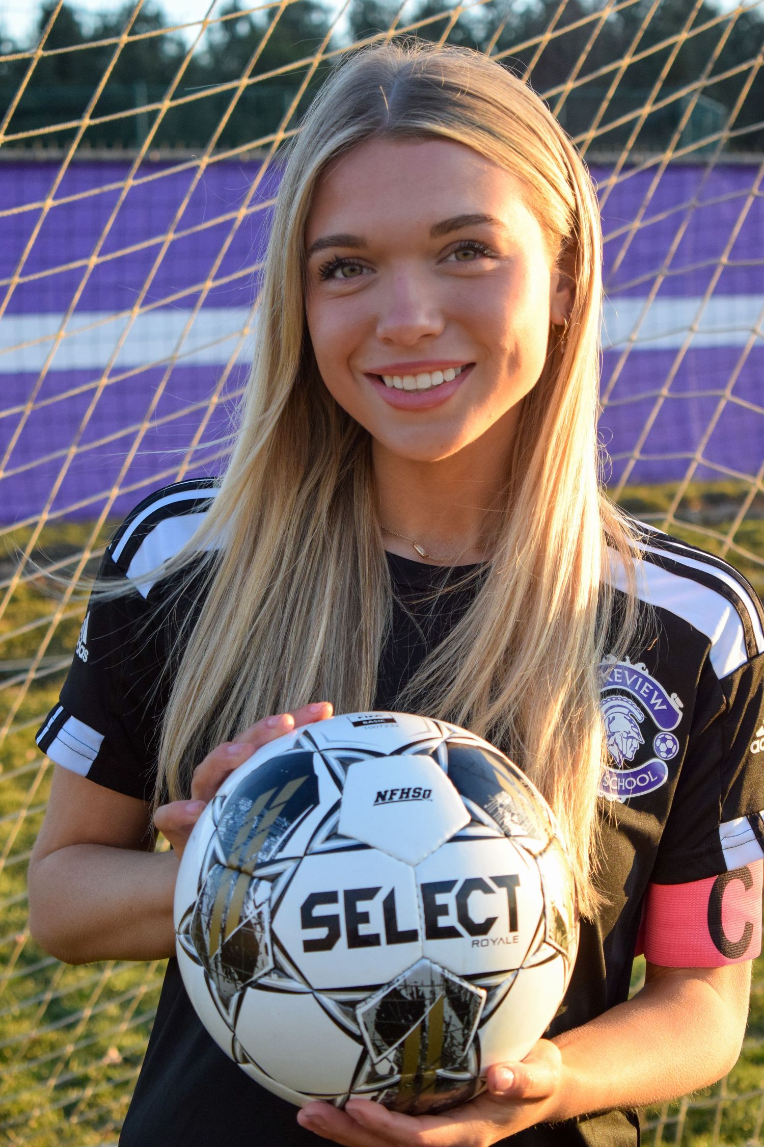 Soccer player poses with Select brand ball in front of goal net during golden hour photo session.