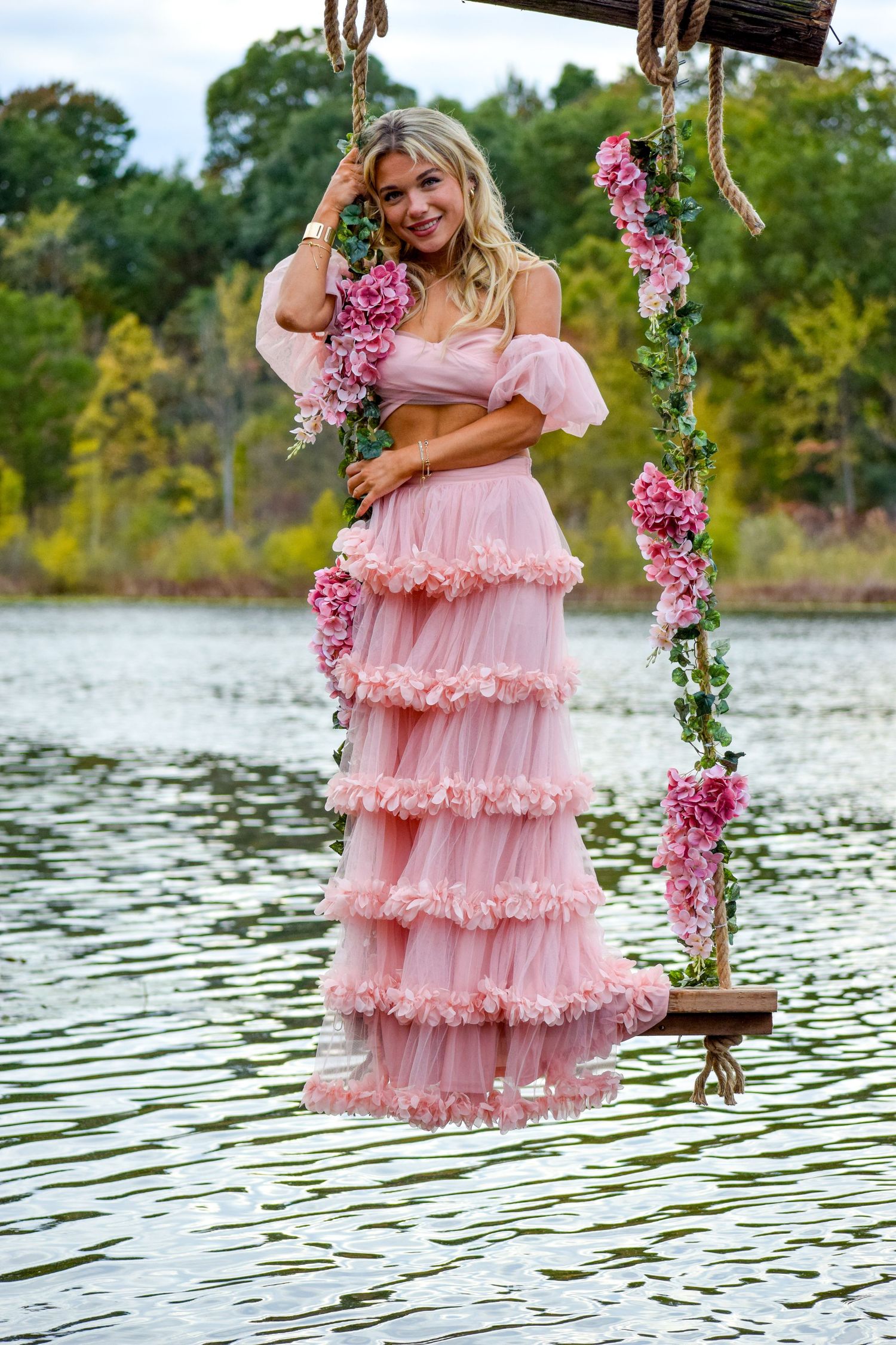 Pink ruffle dress photos on decorated swing over lake with floral accents.