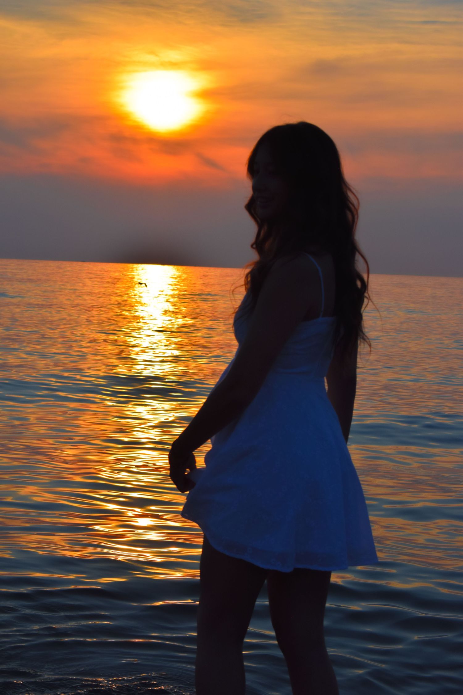 Dramatic silhouette poses against vibrant orange sunset over ocean waters.