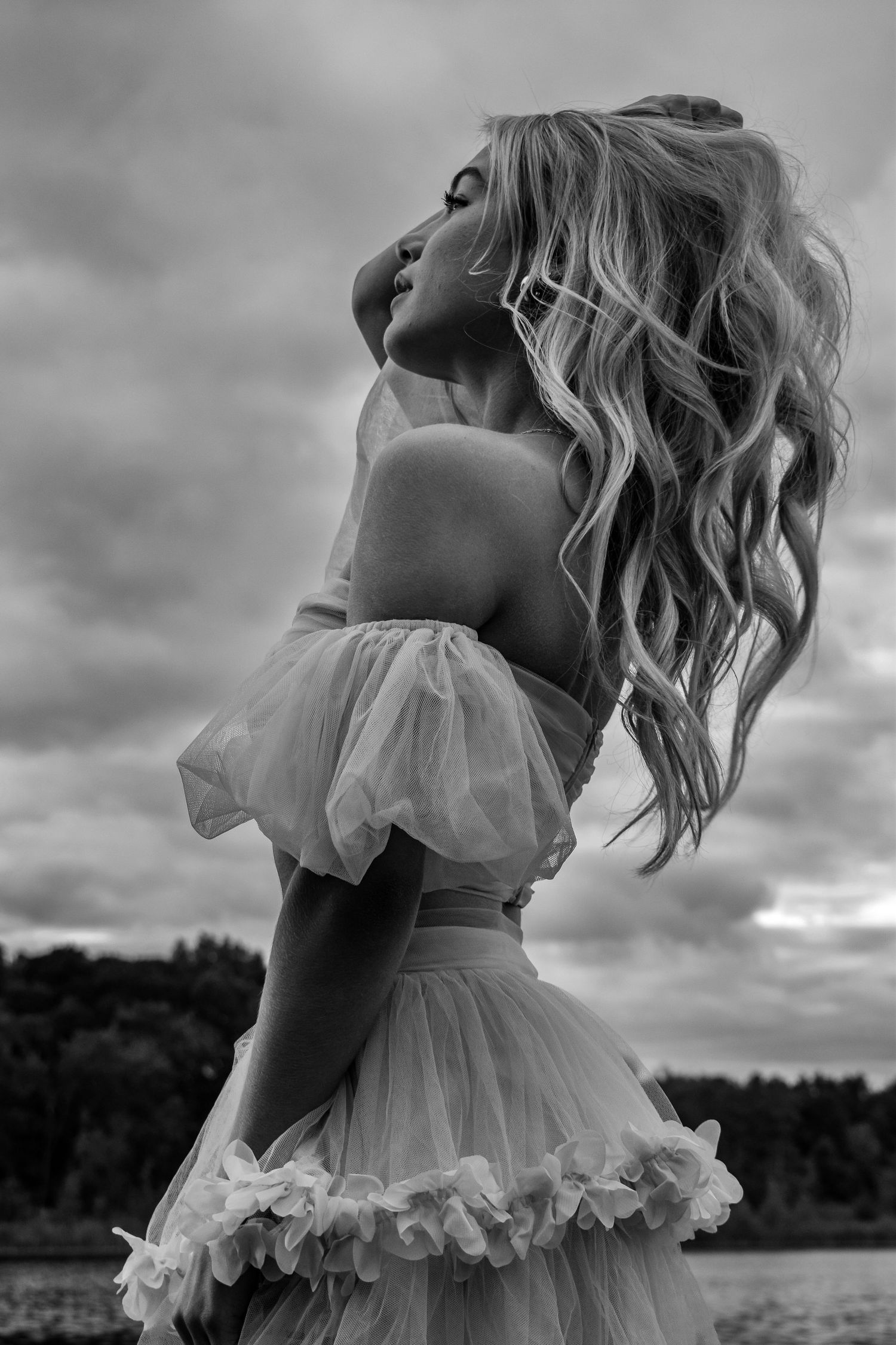 Dreamy black and white portrait series in flowing ruffle dress against cloudy sky.