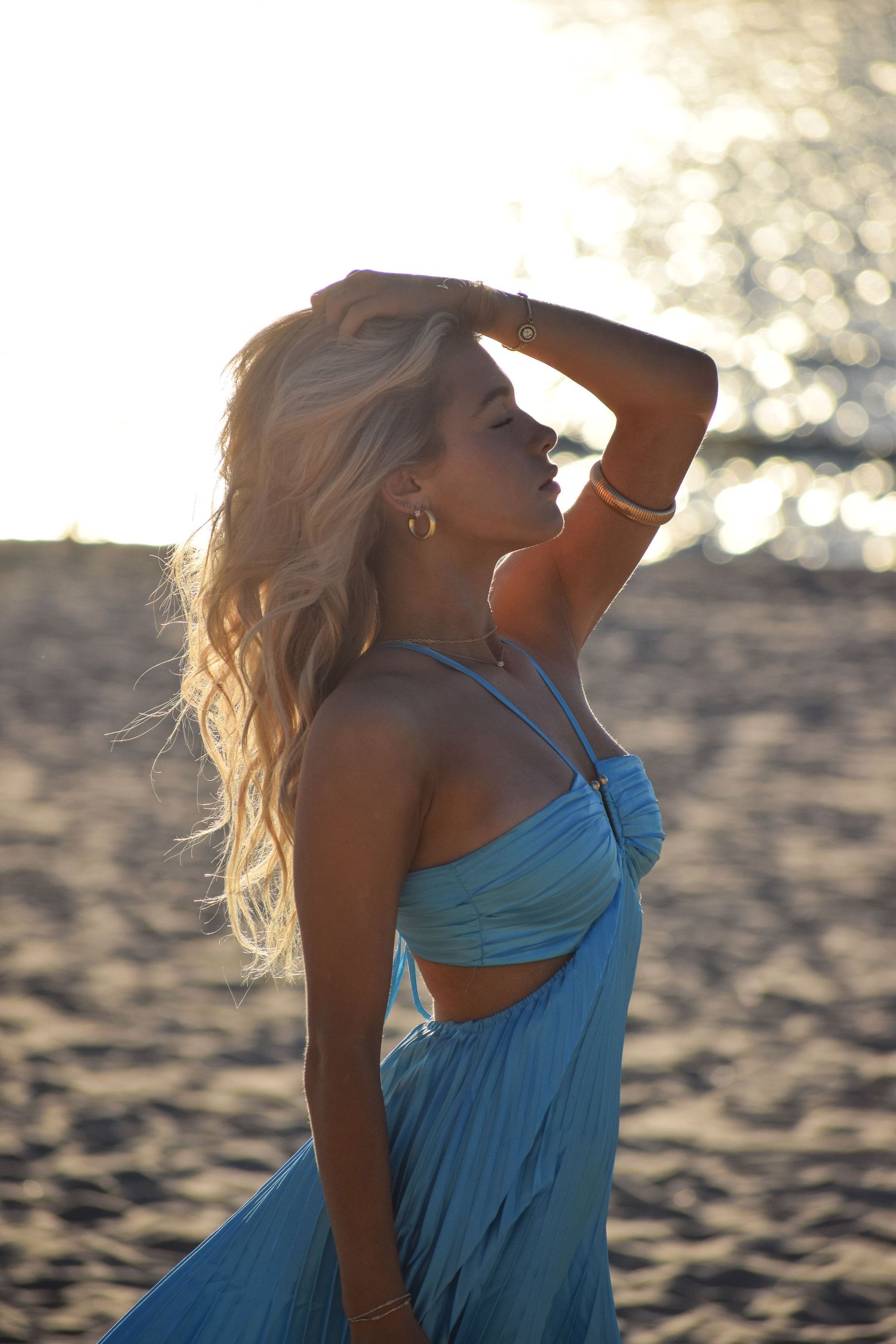 Beach photoshoot with golden lighting showing someone in a flowing blue dress.