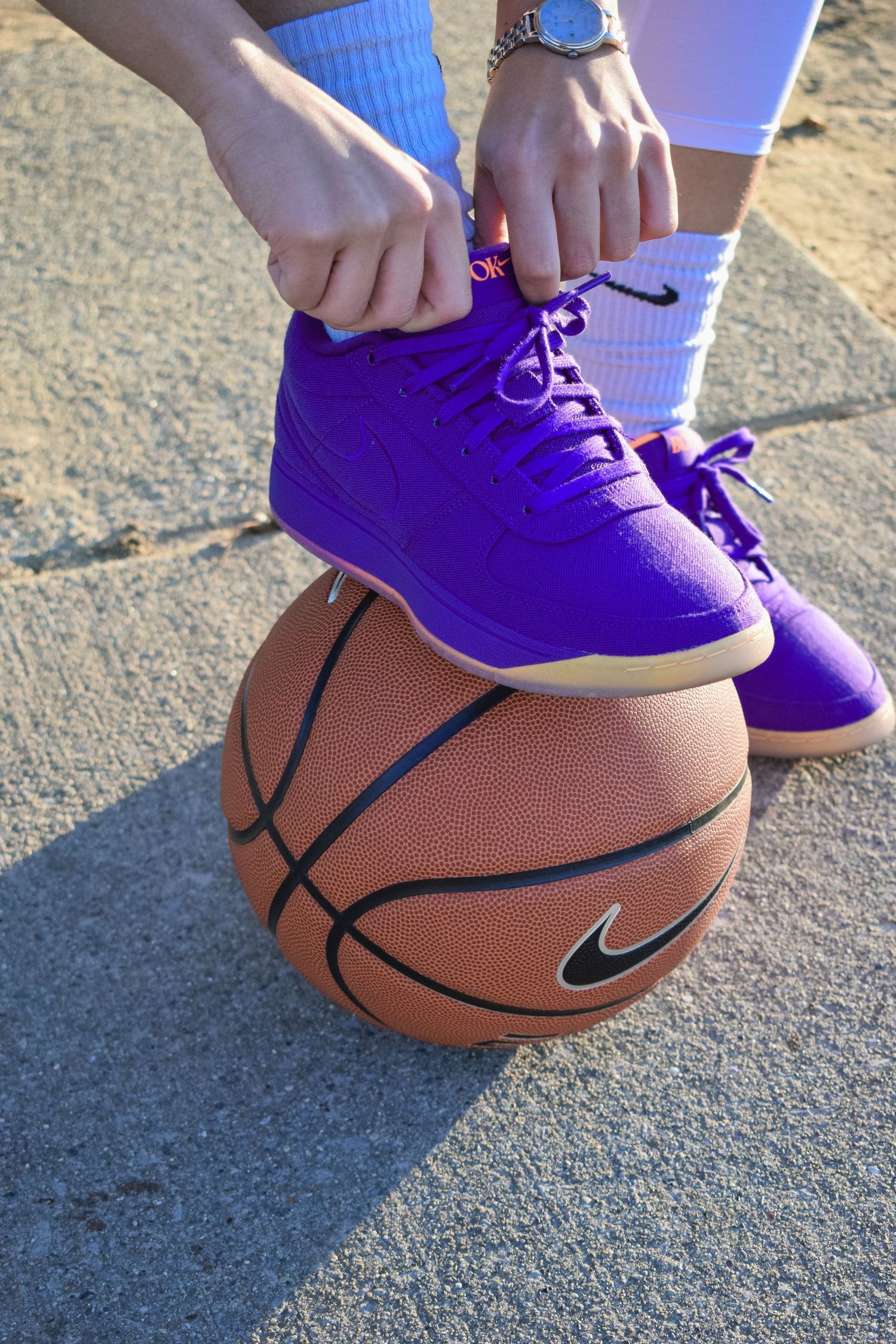 Close-up of purple basketball shoes resting on a basketball on concrete surface.