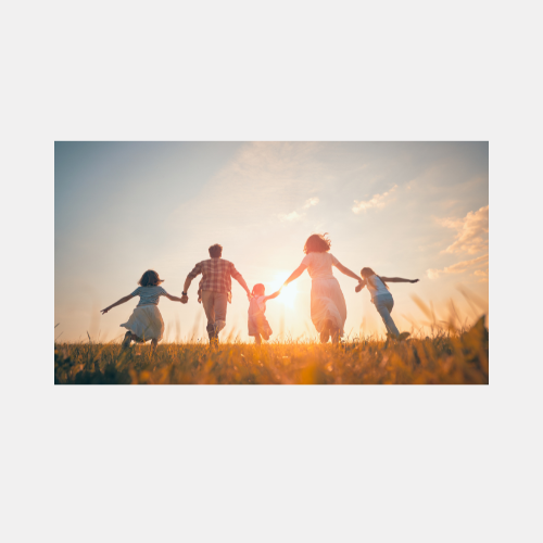 Silhouettes of people holding hands and jumping against a vibrant sunset sky with tall grass in the foreground.