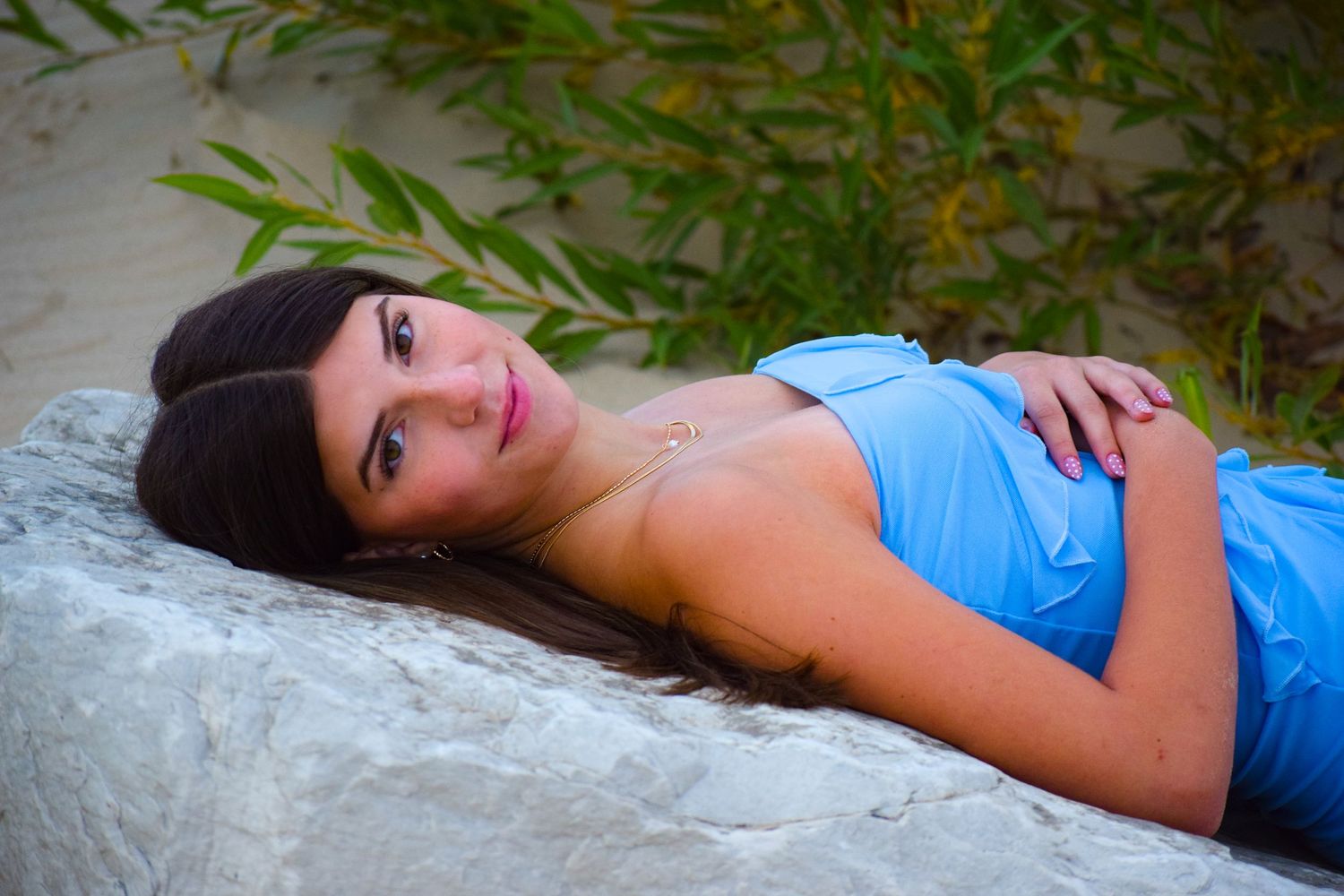 Person in blue dress reclines on natural stone formation during outdoor photo session.