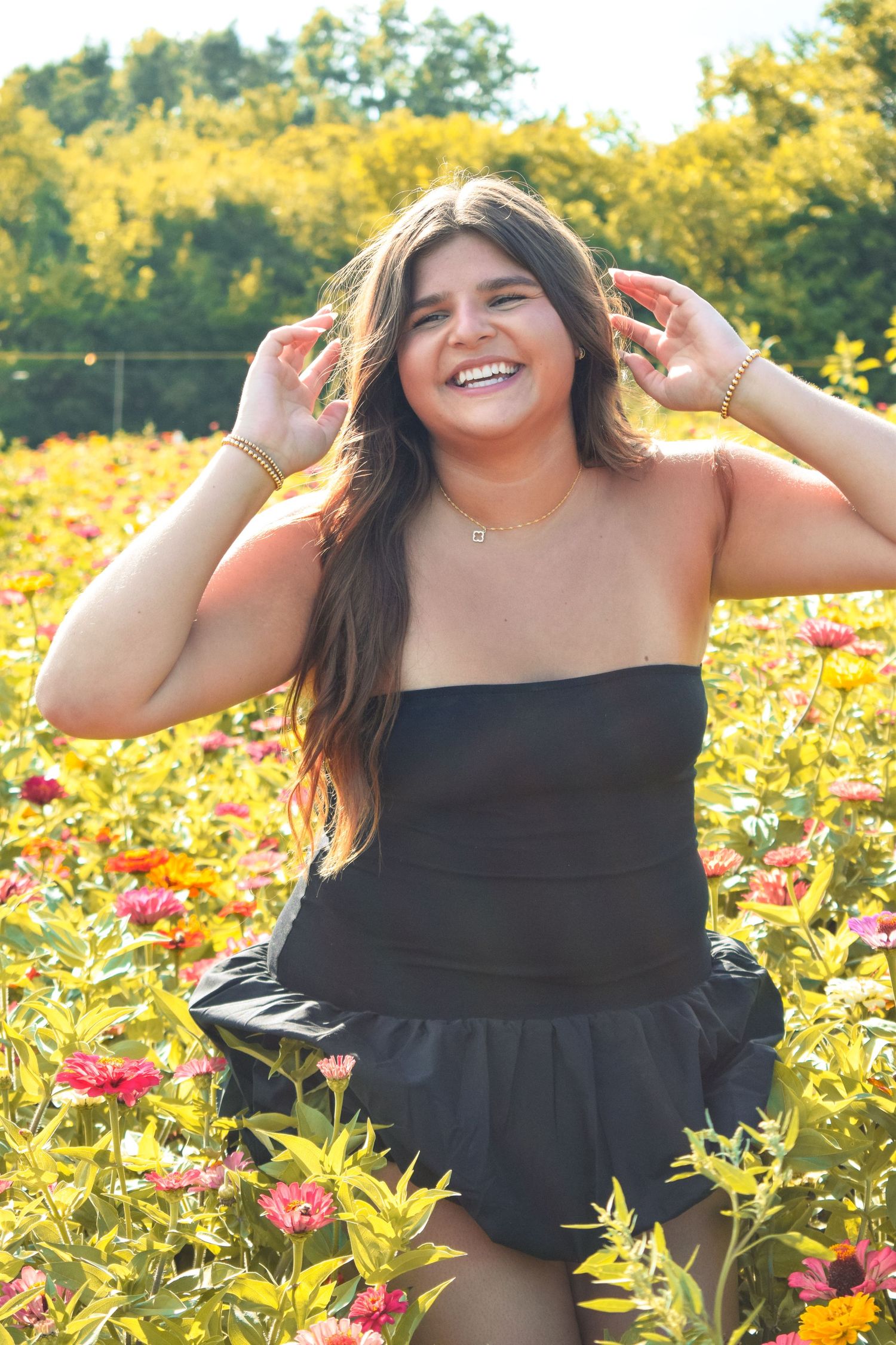 Woman in black dress laughs joyfully while posing in flower garden during golden hour.
