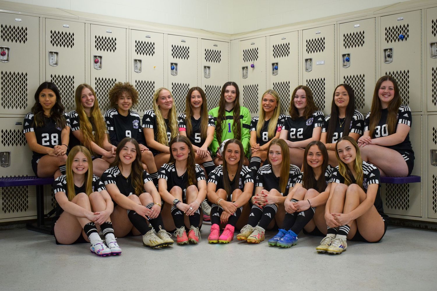 Soccer team members sit together in locker room for group photo.