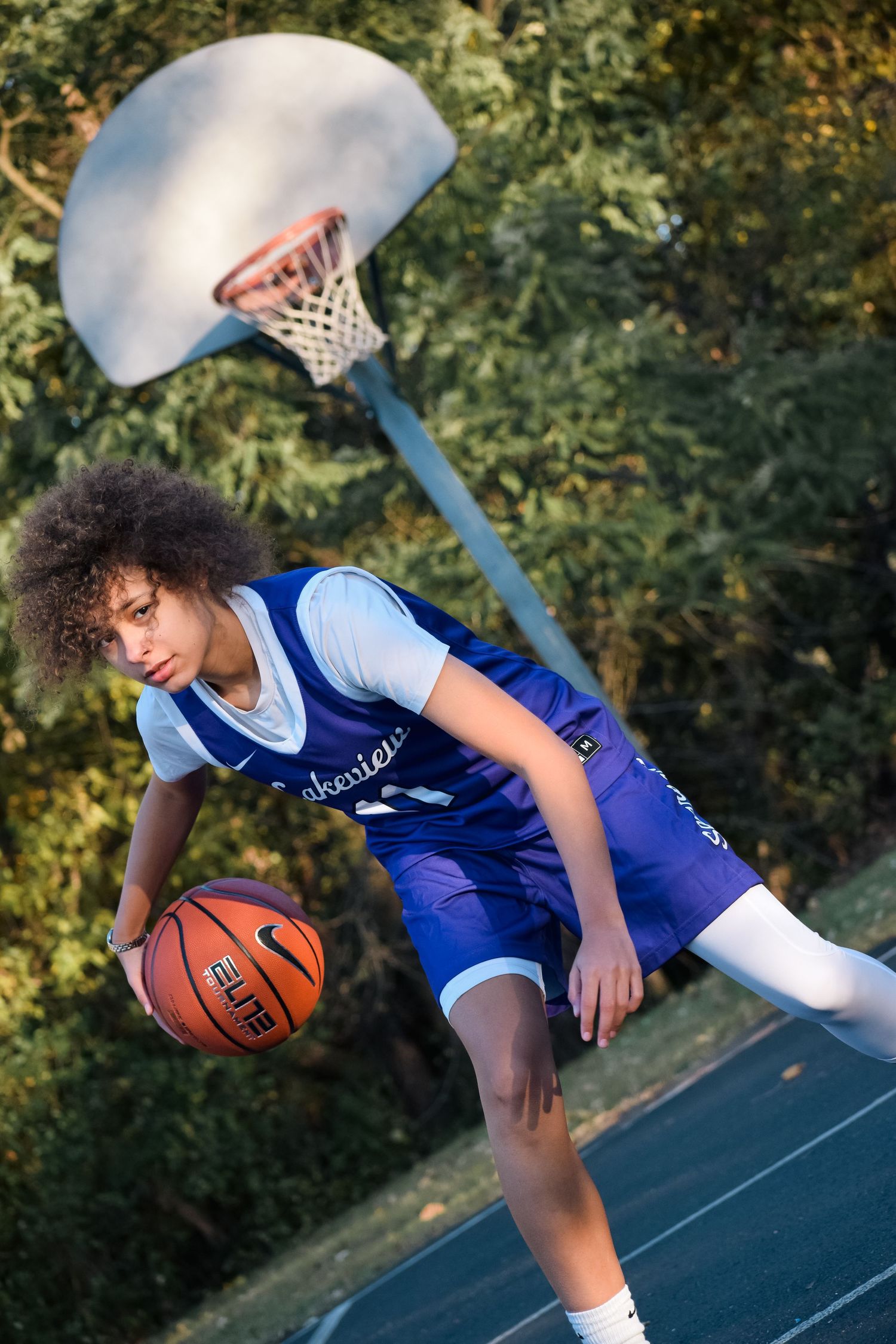 Basketball player in blue jersey demonstrates dribbling moves on an outdoor court.