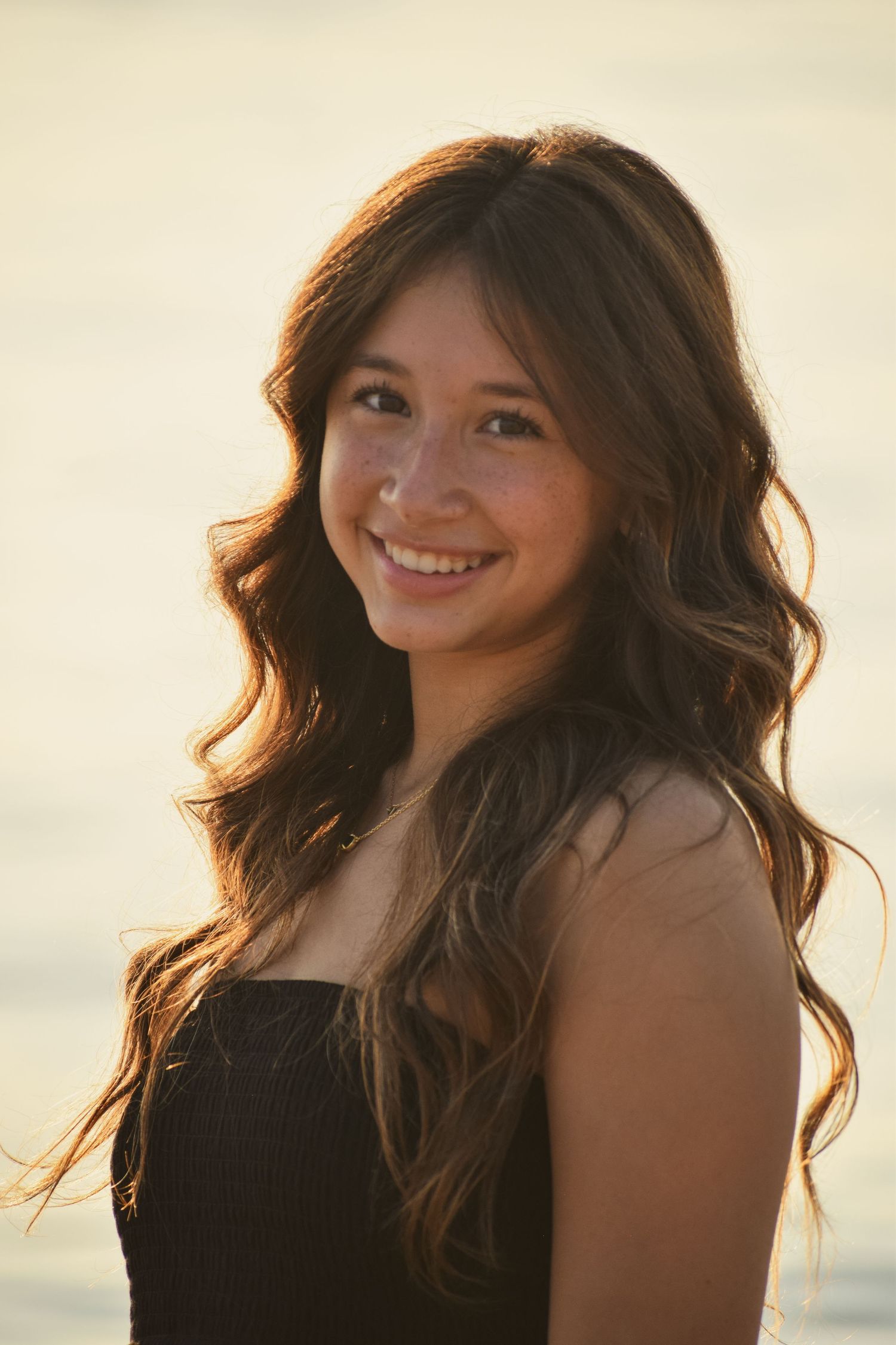 A series of five photos showing a woman with flowing dark hair smiling at sunset by the ocean.