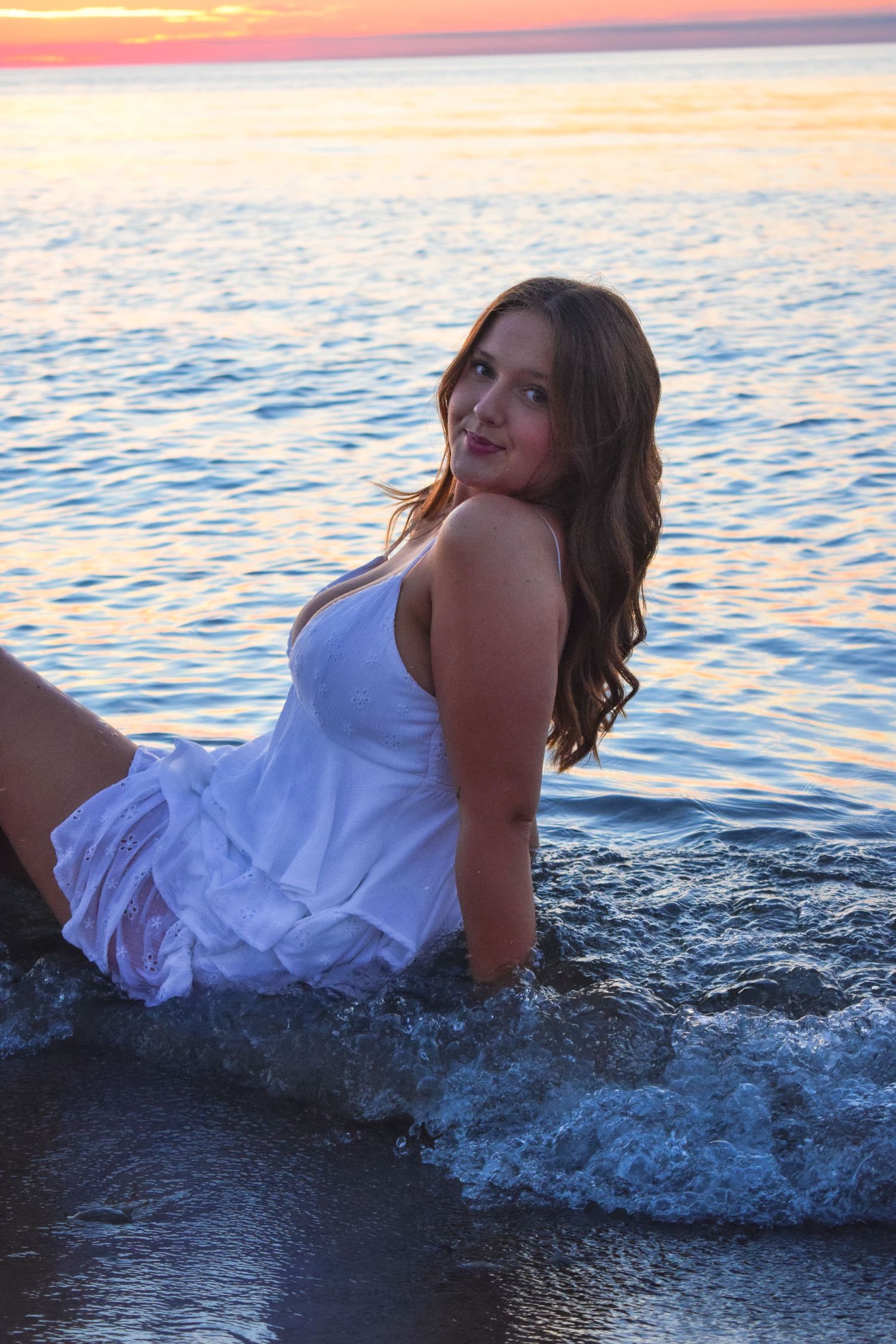 White dress beach photoshoot with waves splashing during sunset.