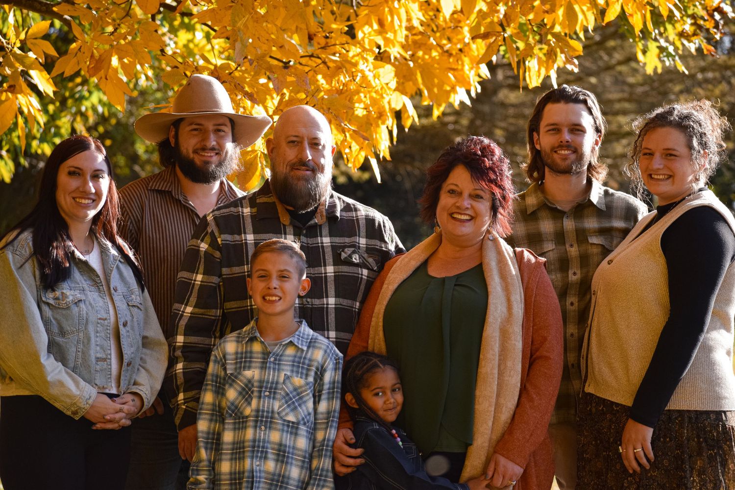 Large group portrait with warm autumn colors and golden sunlight filtering through trees.