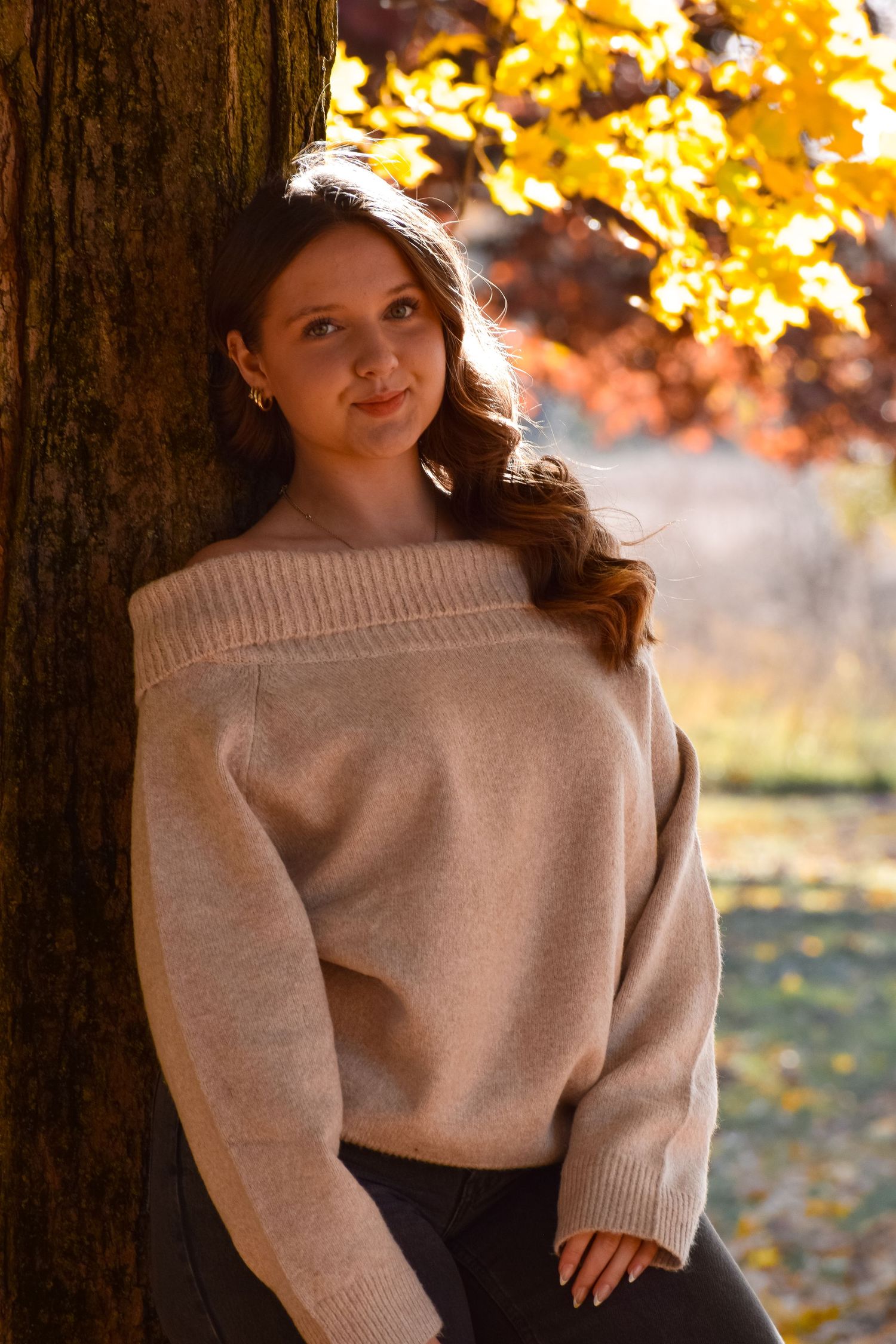 Fall fashion photography with beige sweater against autumn trees and leaves.