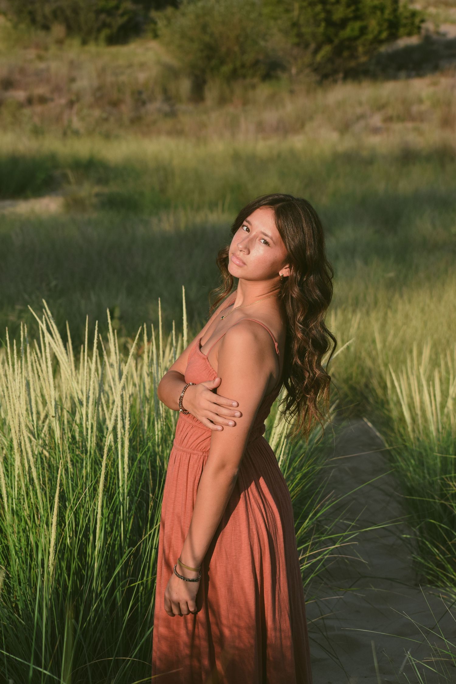 Artistic portrait in coral dress against tall grass during golden hour.